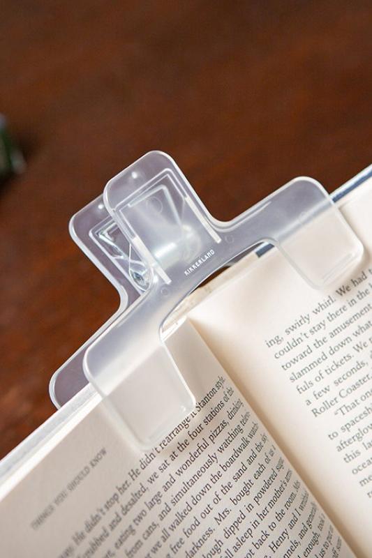Clear book clip holding open a book on a wooden surface