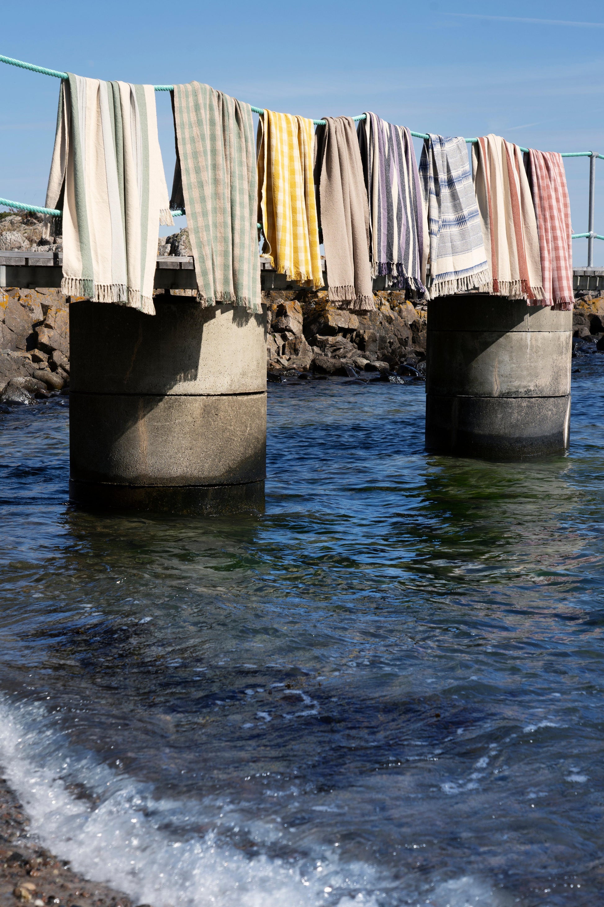 Multiple colorful striped and patterned towels hanging to dry on a railing over the ocean.