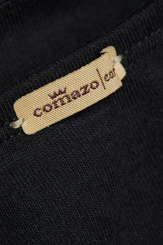 Close-up of a beige Comazo organic cotton clothing label sewn onto black fabric.