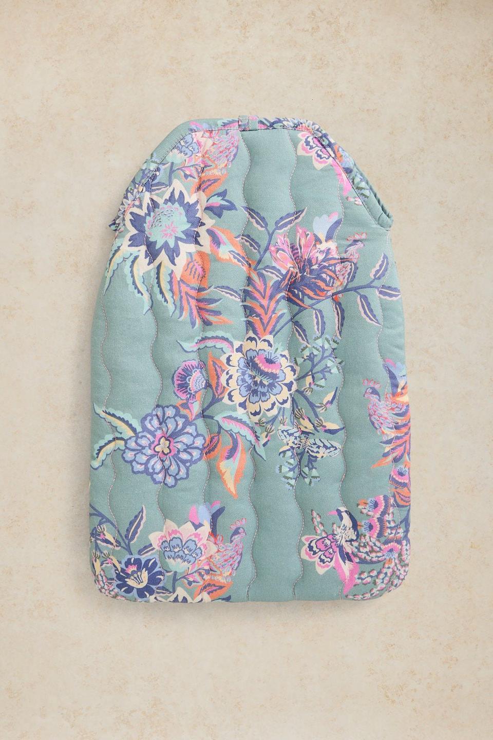 A quilted fabric pouch or cover with a floral print in shades of teal, pink, purple, and orange, displayed flat against a textured beige background.