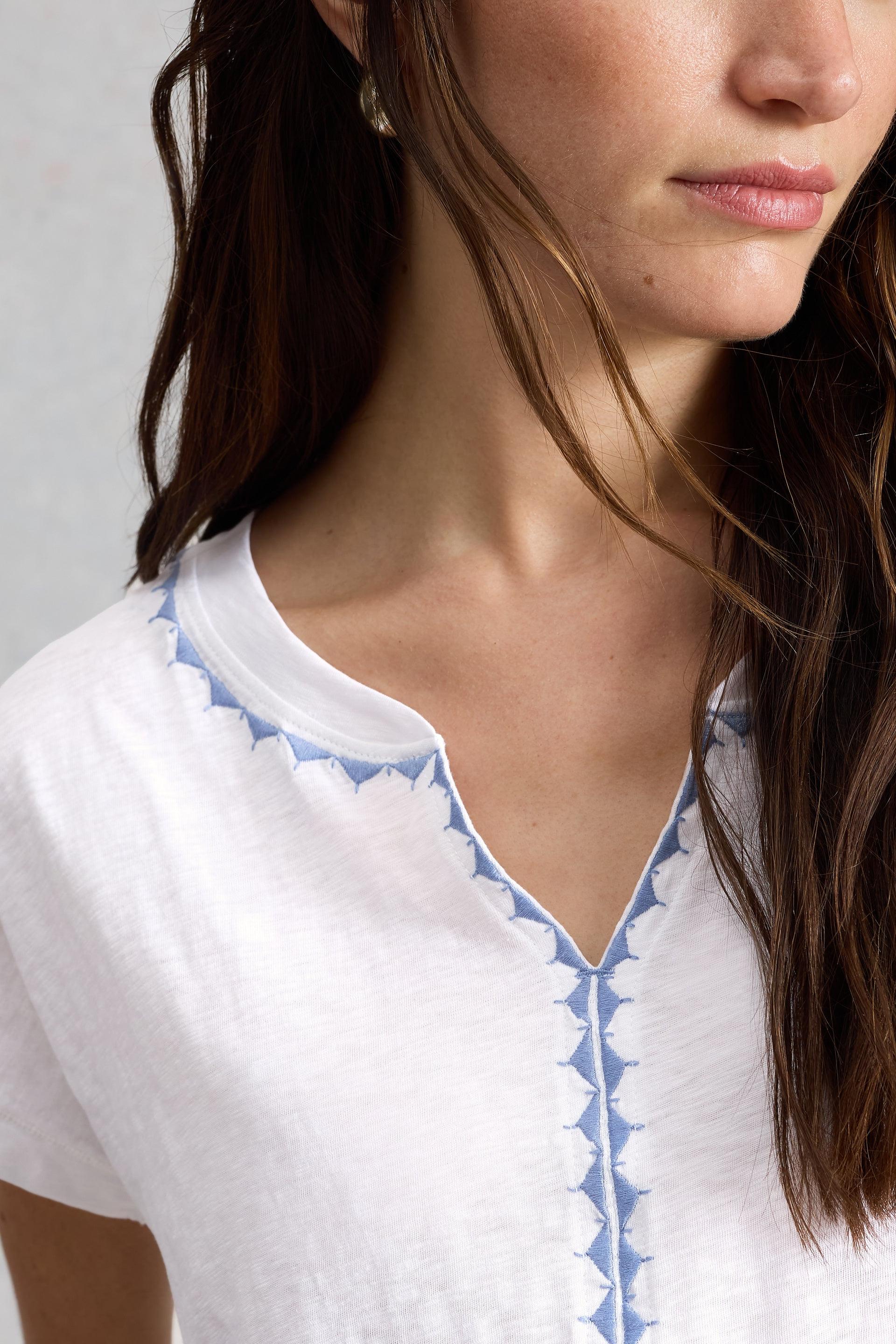 Close-up of a person wearing a white t-shirt with blue trim and notch neckline on a neutral background