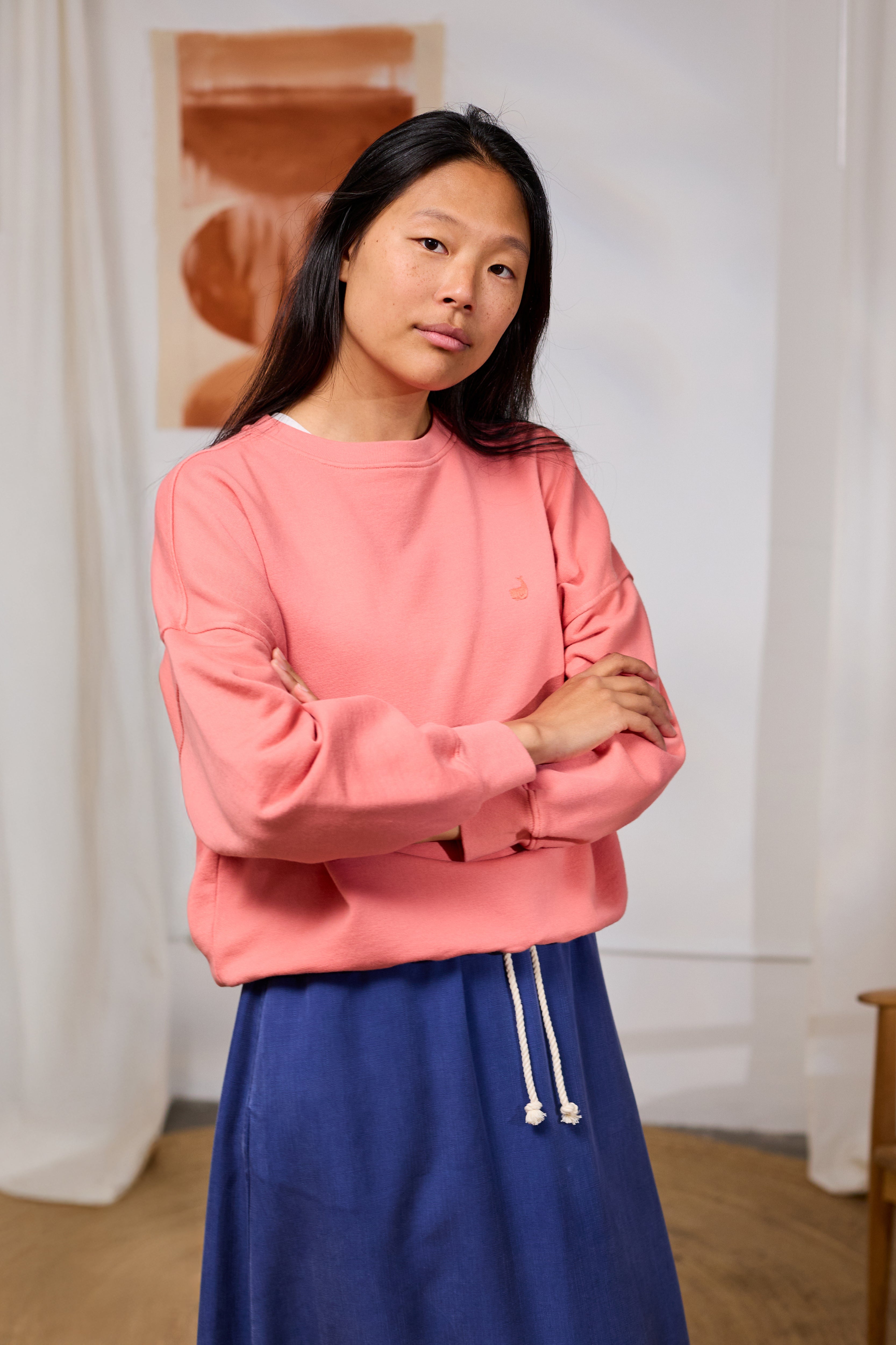 Person wearing a pink cotton sweatshirt and blue pants standing indoors with a neutral background