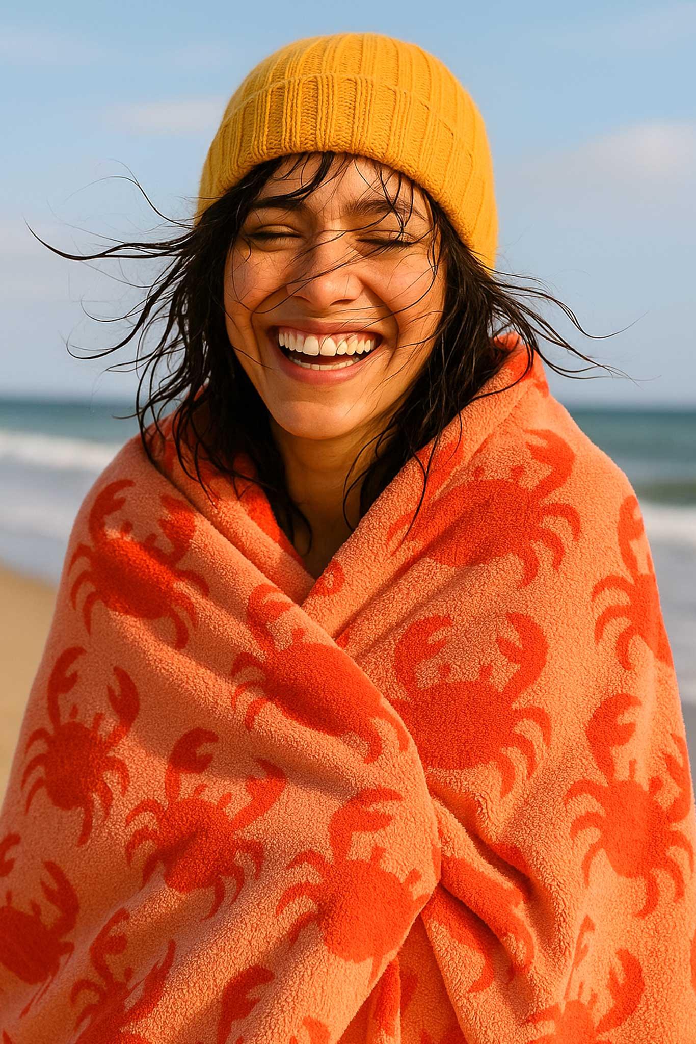 Person wrapped in a red crab-patterned towel on a beach