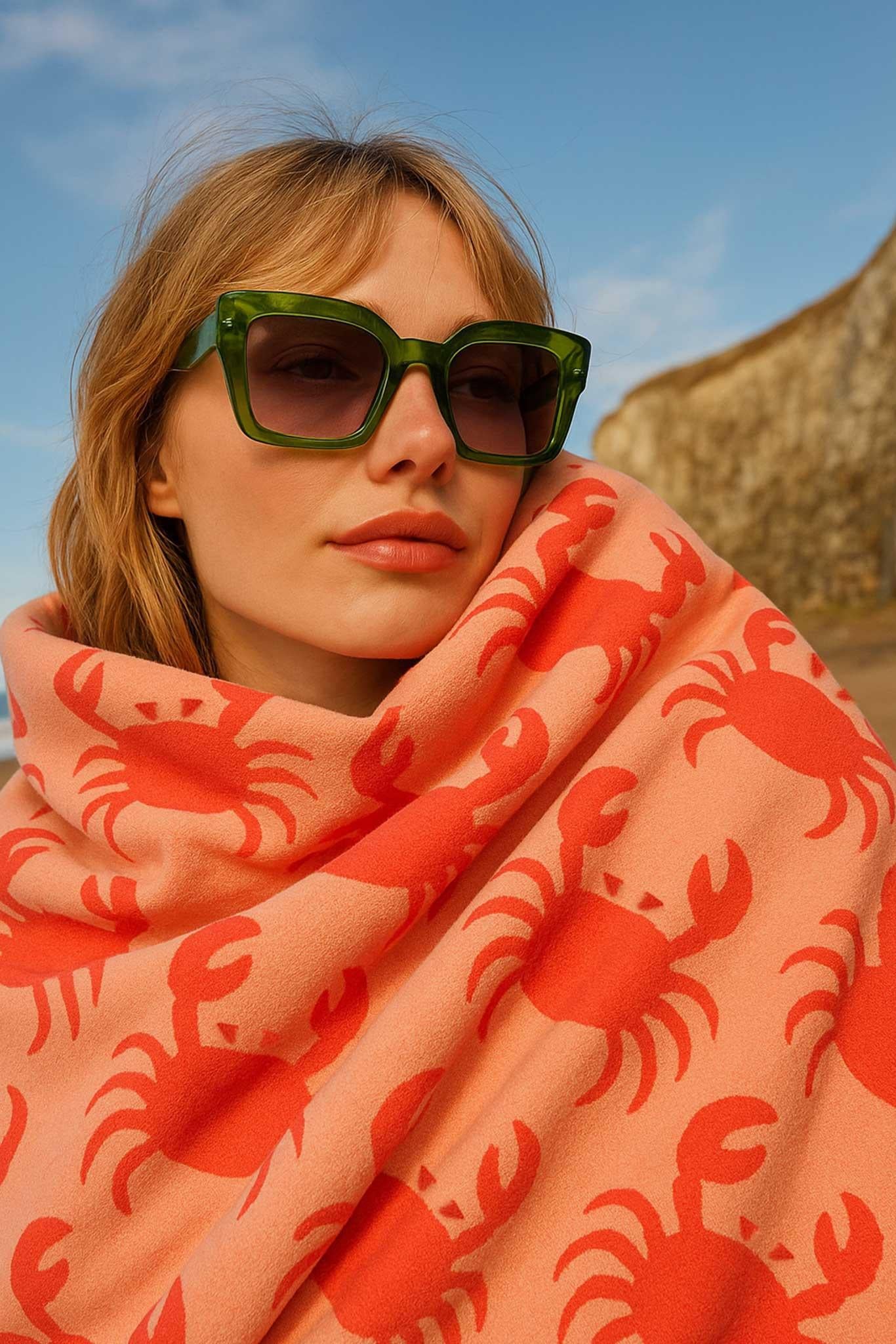 Woman wearing a pink towel with red crab patterns on a beach.