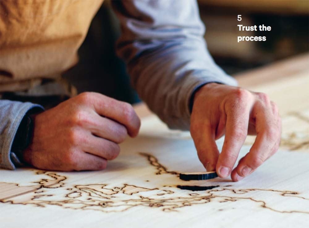 Close-up of a craftsman's hands working on a piece of wood with intricate pyrography designs
