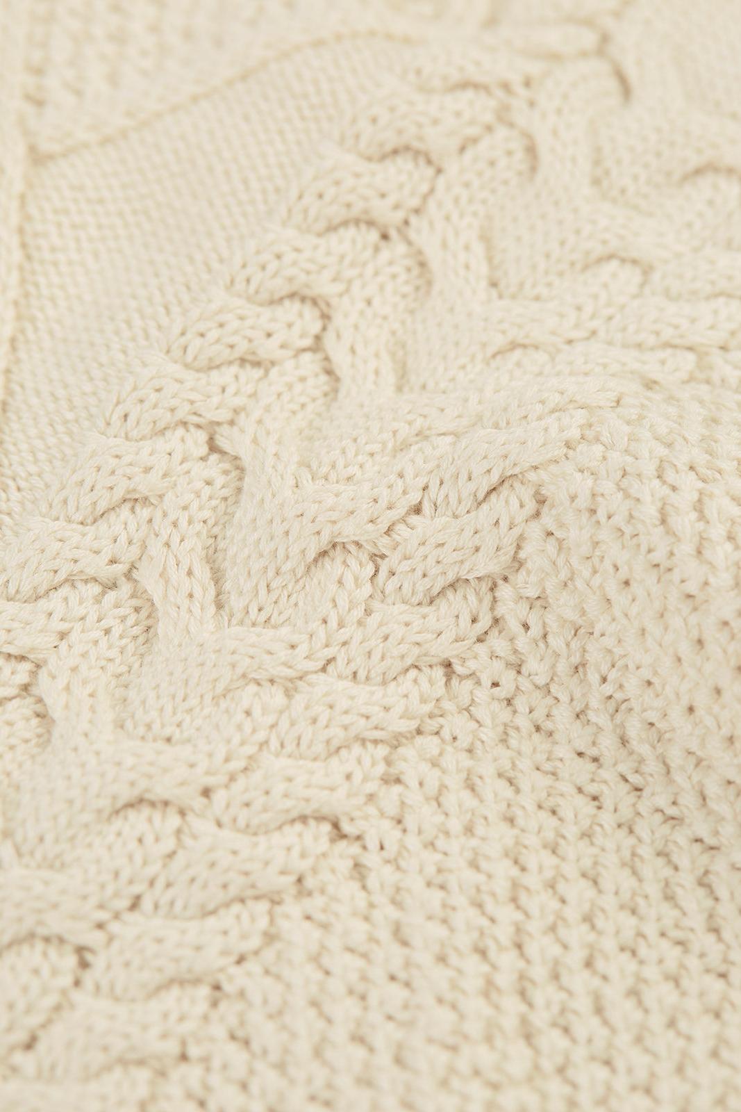 Close-up of a cream-colored organic cotton jumper featuring a traditional cable knit Aran pattern.