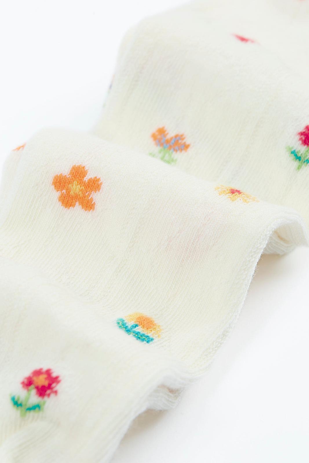 Cream organic cotton baby tights featuring a delicate colourful floral pattern, isolated on a white background.
