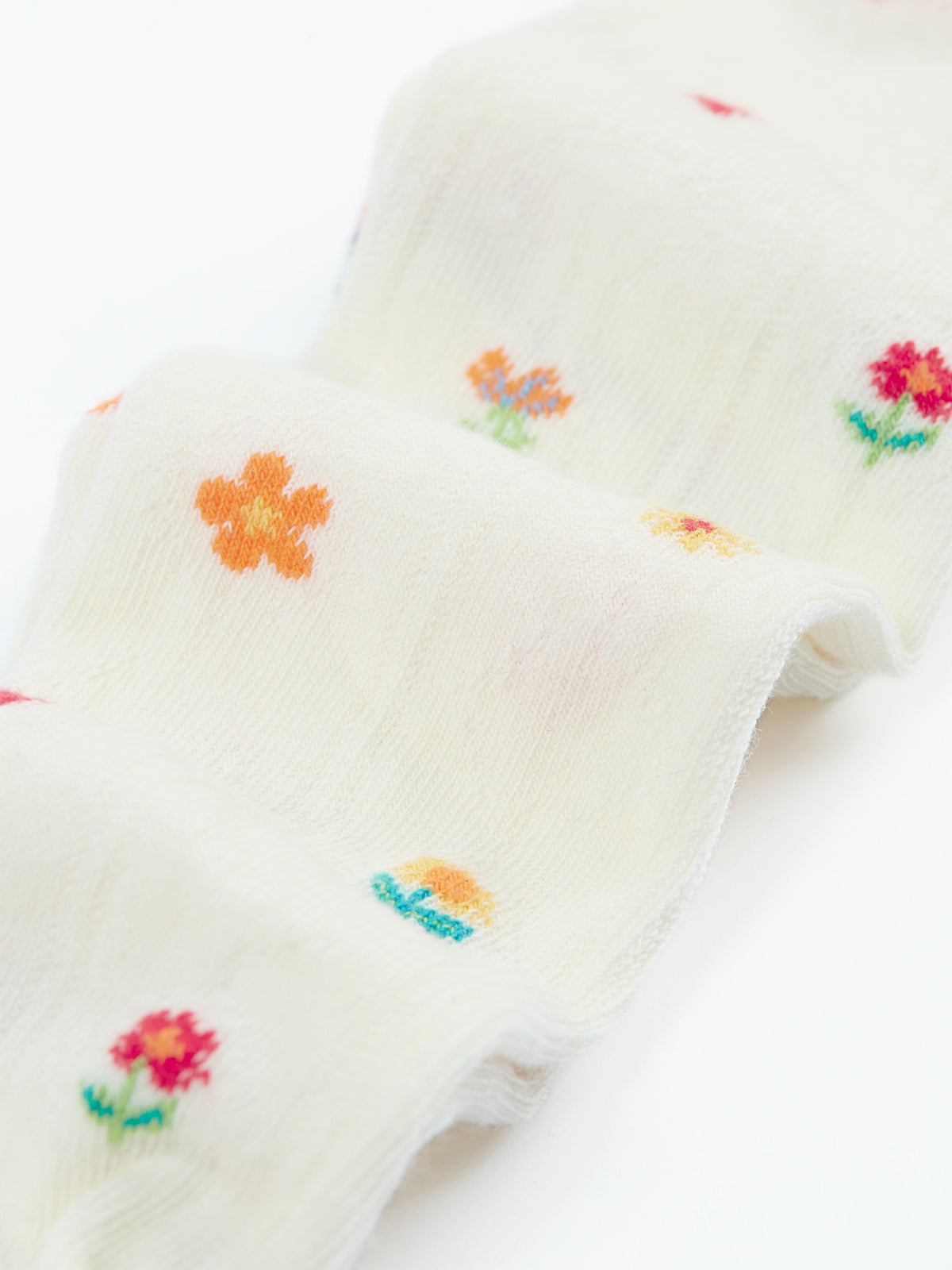 Cream organic cotton baby tights featuring a delicate colourful floral pattern, isolated on a white background.