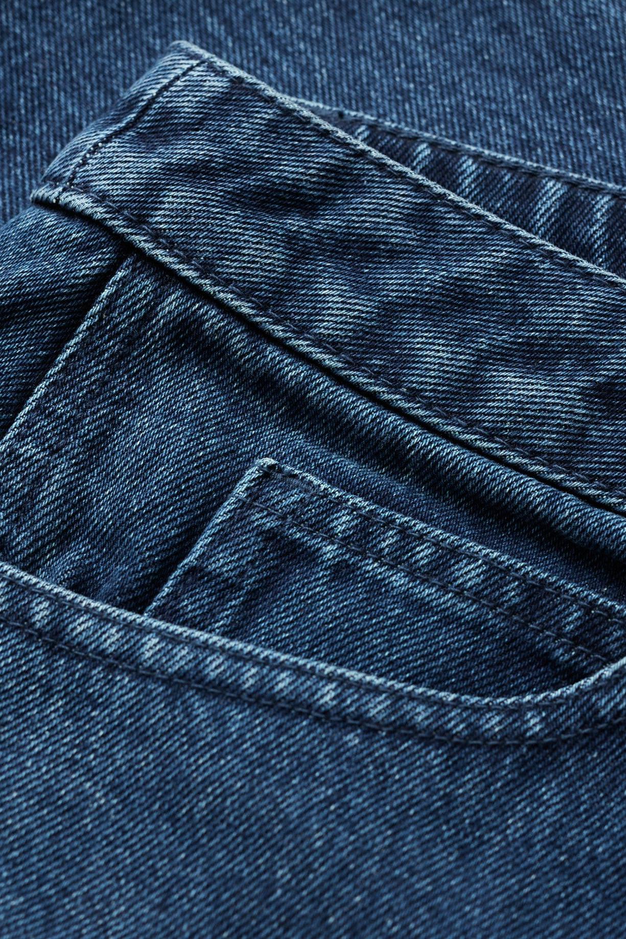 Close-up of dark blue denim fabric showing the texture of a back pocket with detailed stitching.
