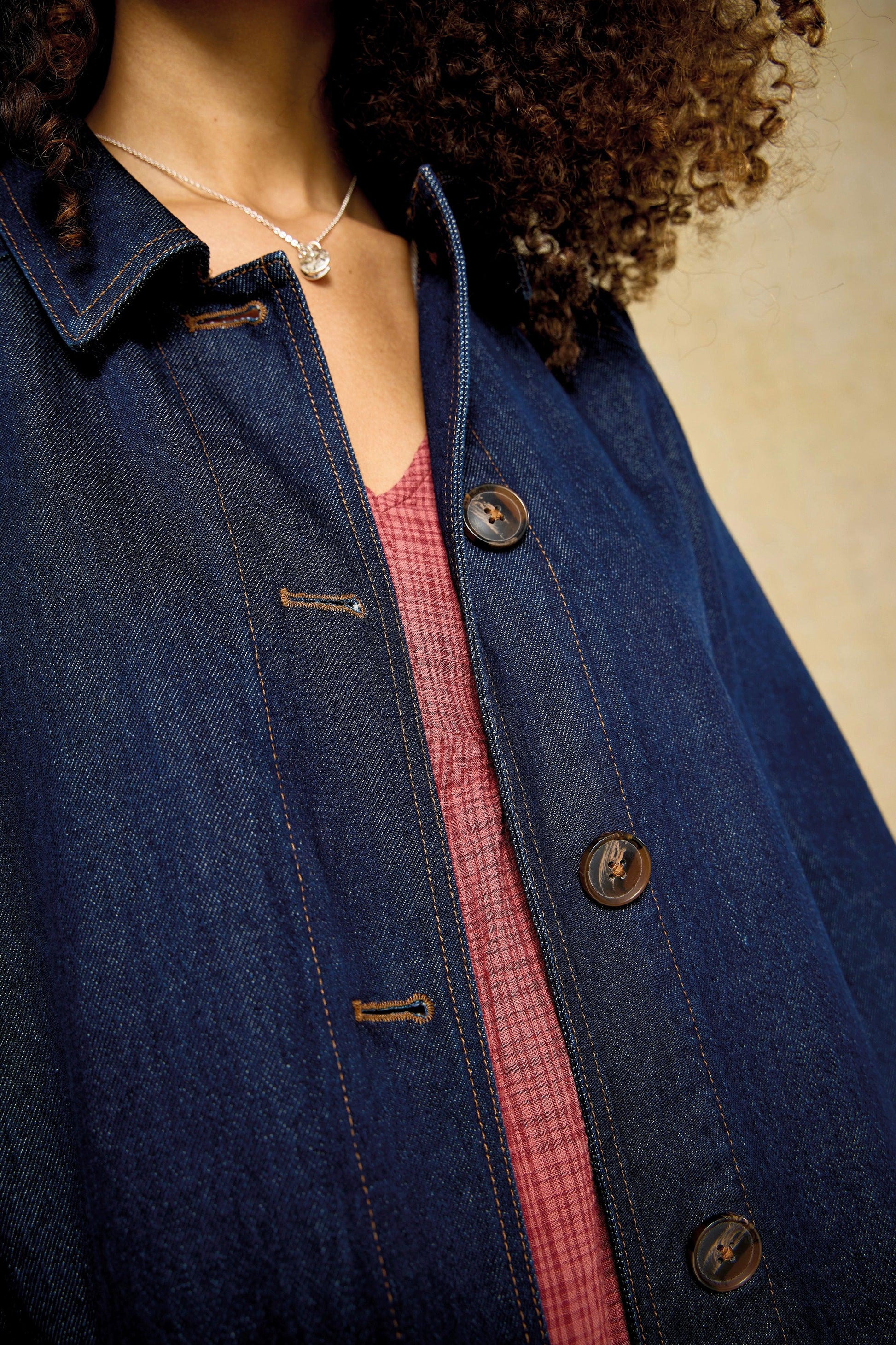 Close-up of a person wearing a dark blue denim jacket layered over a reddish textured organic cotton top