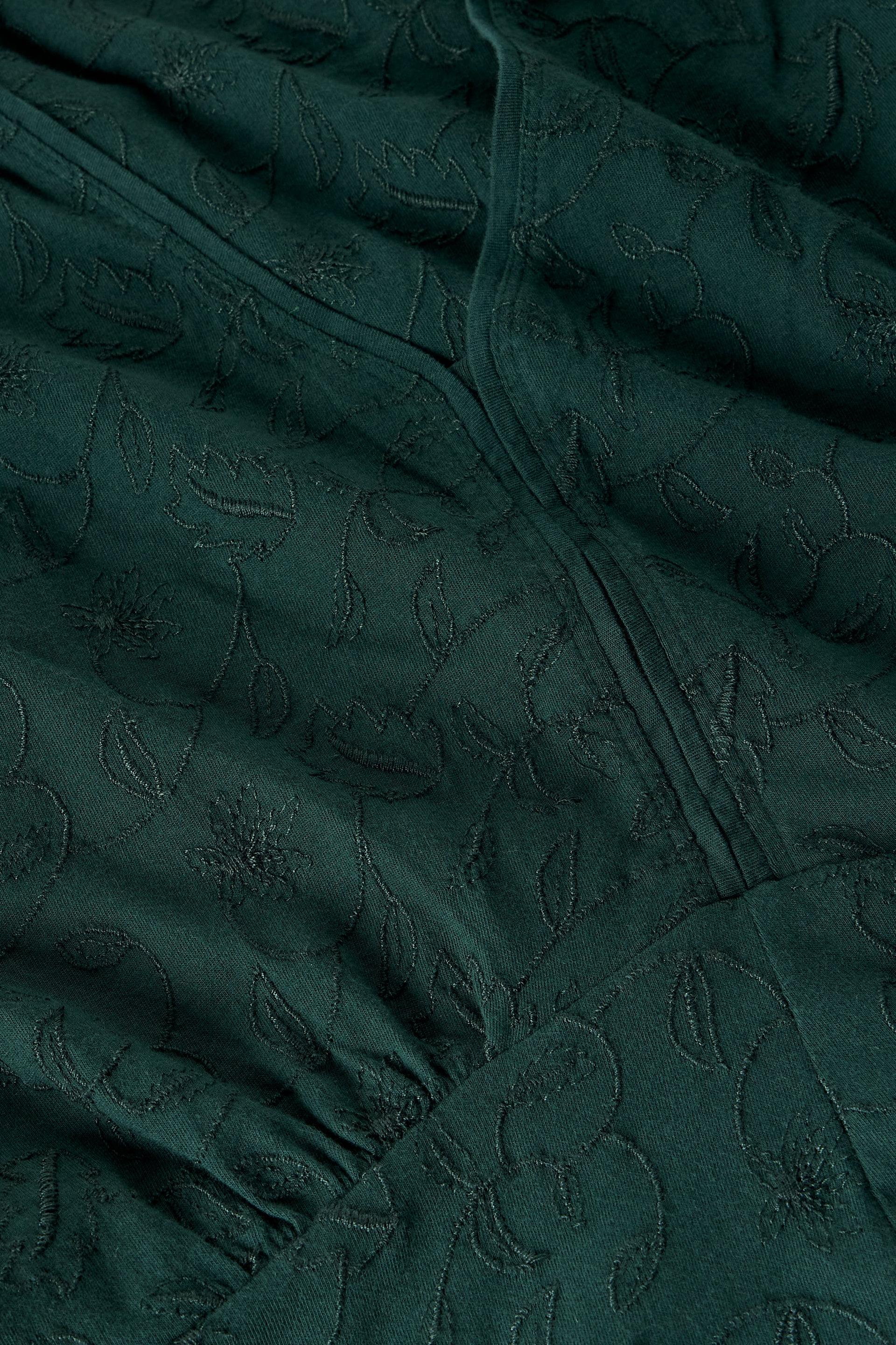 Close-up of a dark green fabric with an embossed floral pattern and gathered seams.
