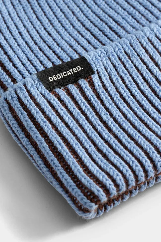 Close-up of a blue ribbed cotton beanie with a black Dedicated brand label.