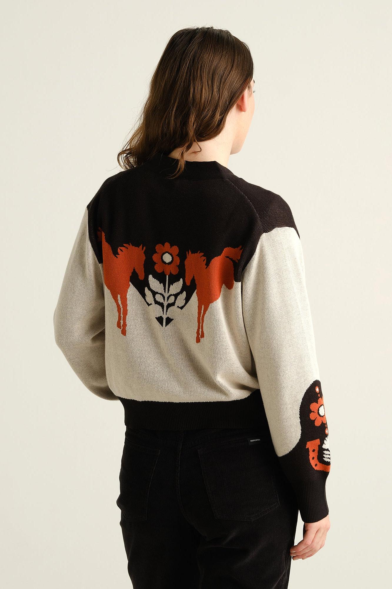 A model viewed from the back wearing a color-blocked knit sweater with a large orange and black horse graphic across the back and a black sleeve graphic, paired with black pants against a plain off-white background.