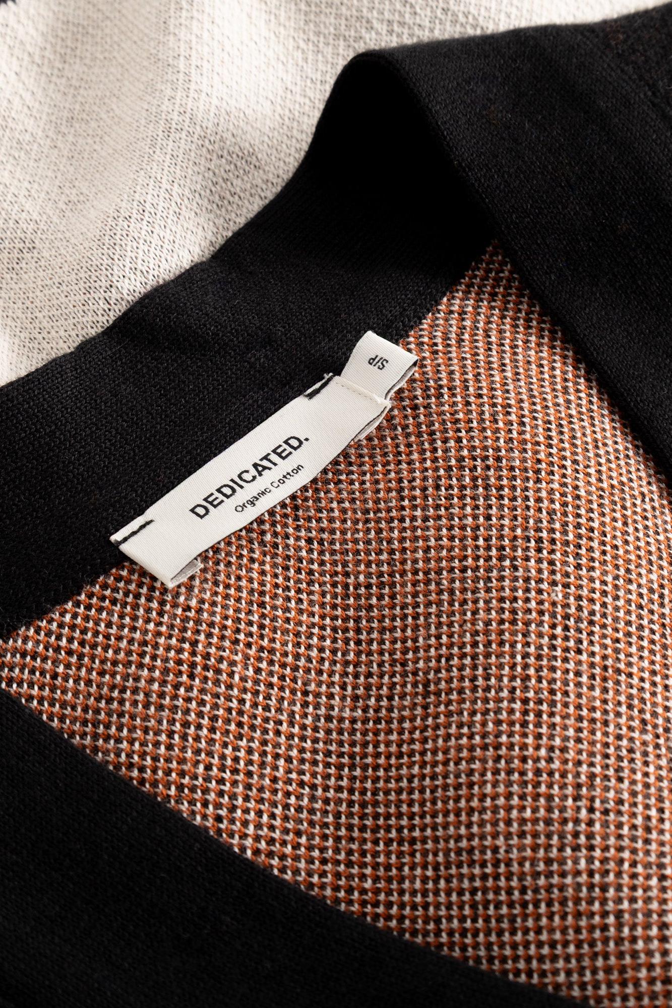 Close-up of a black knit garment with a white interior lining and a visible sewn-on label reading DEDICATED. Organic Cotton