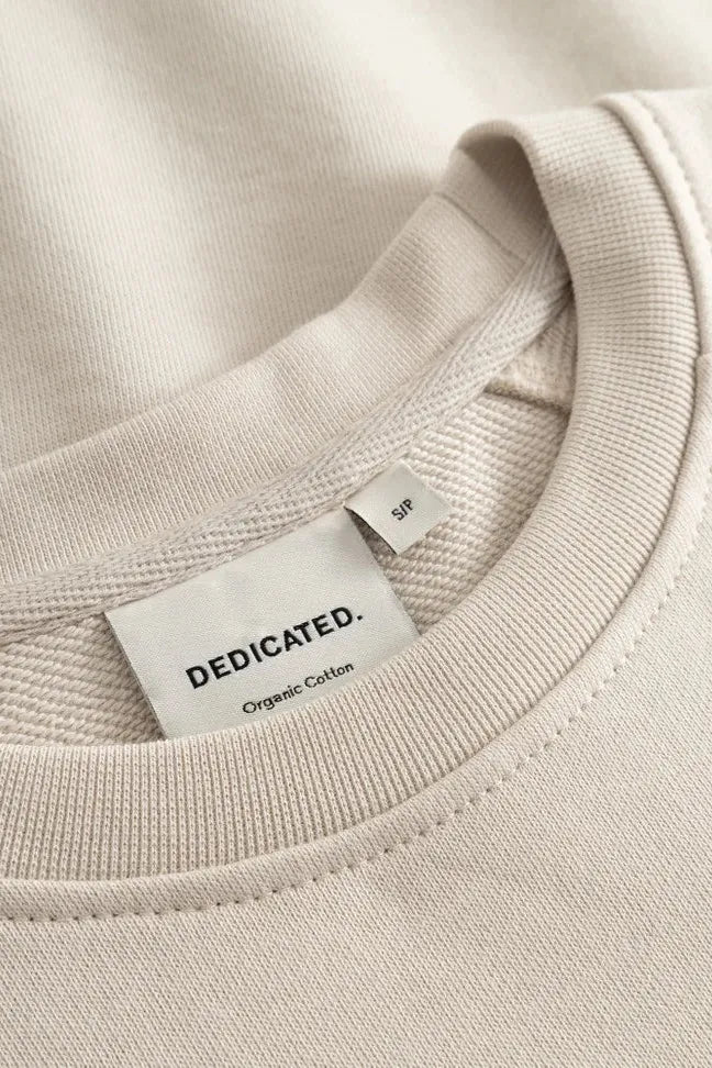 Close up of the neck label on a beige Dedicated brand organic cotton women's sweatshirt.