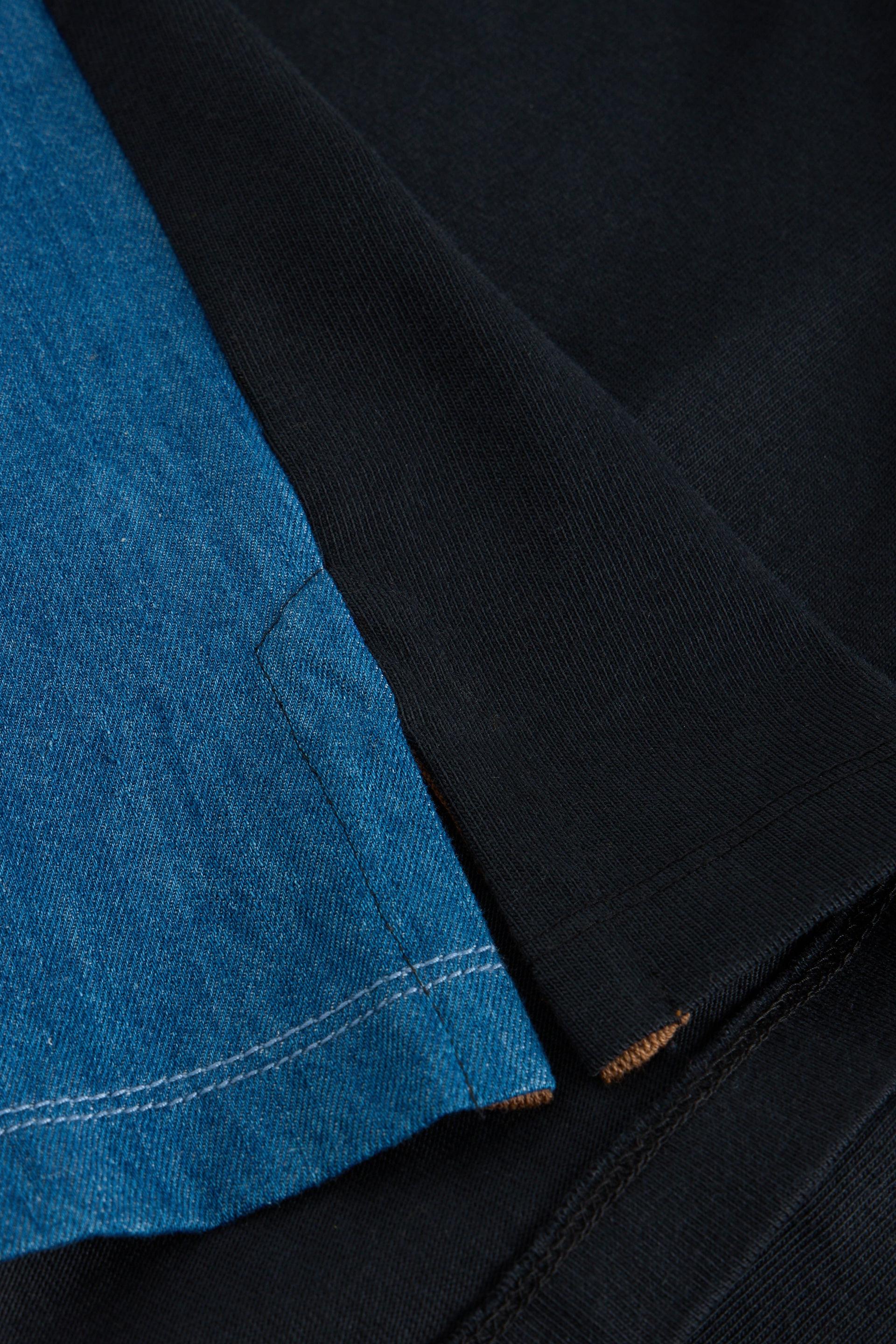 Close-up view of blue denim fabric layered over a black organic cotton textile with visible stitching