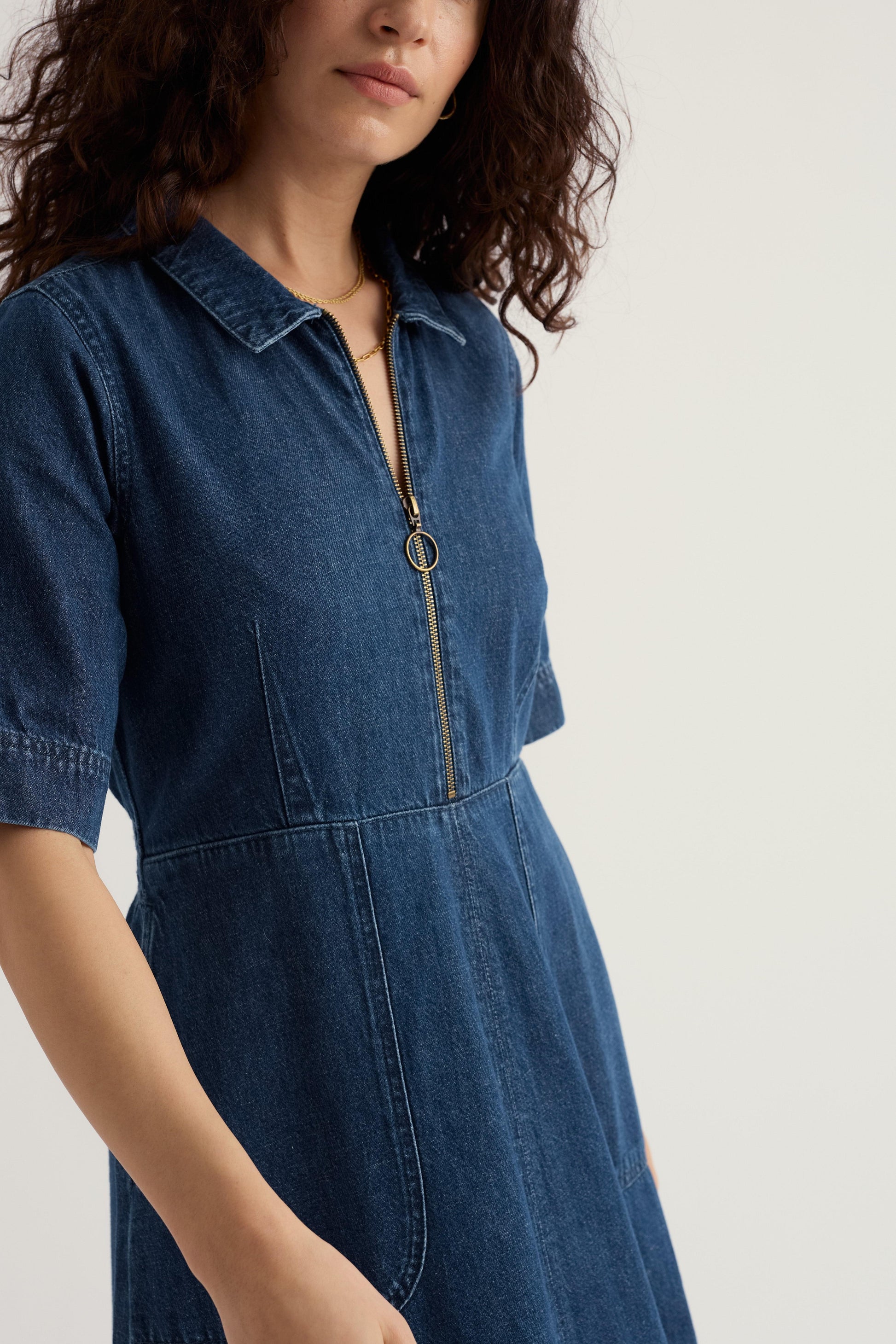 Woman wearing a blue denim dress with a zipper on a light background