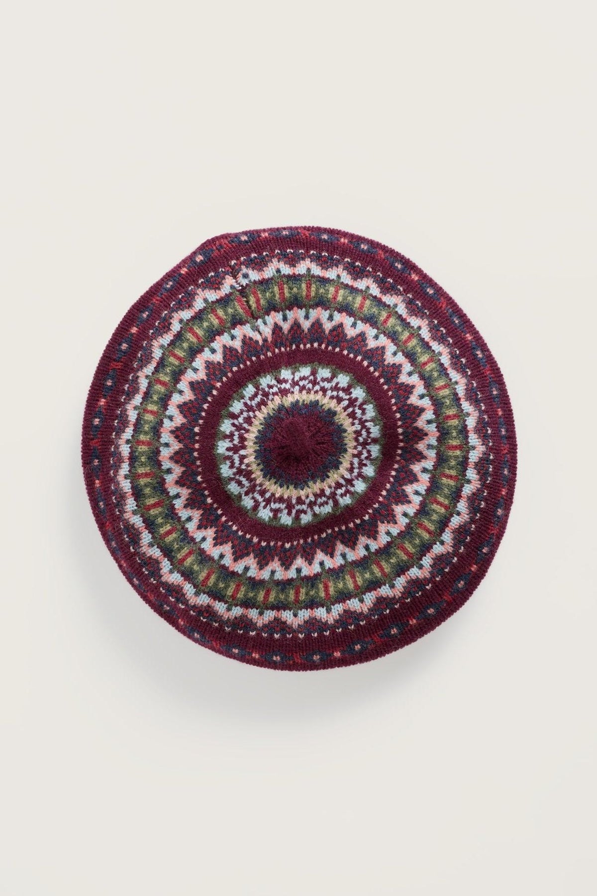 A round, knitted wool beret featuring a colorful Fair Isle pattern in shades of burgundy, olive, and cream.