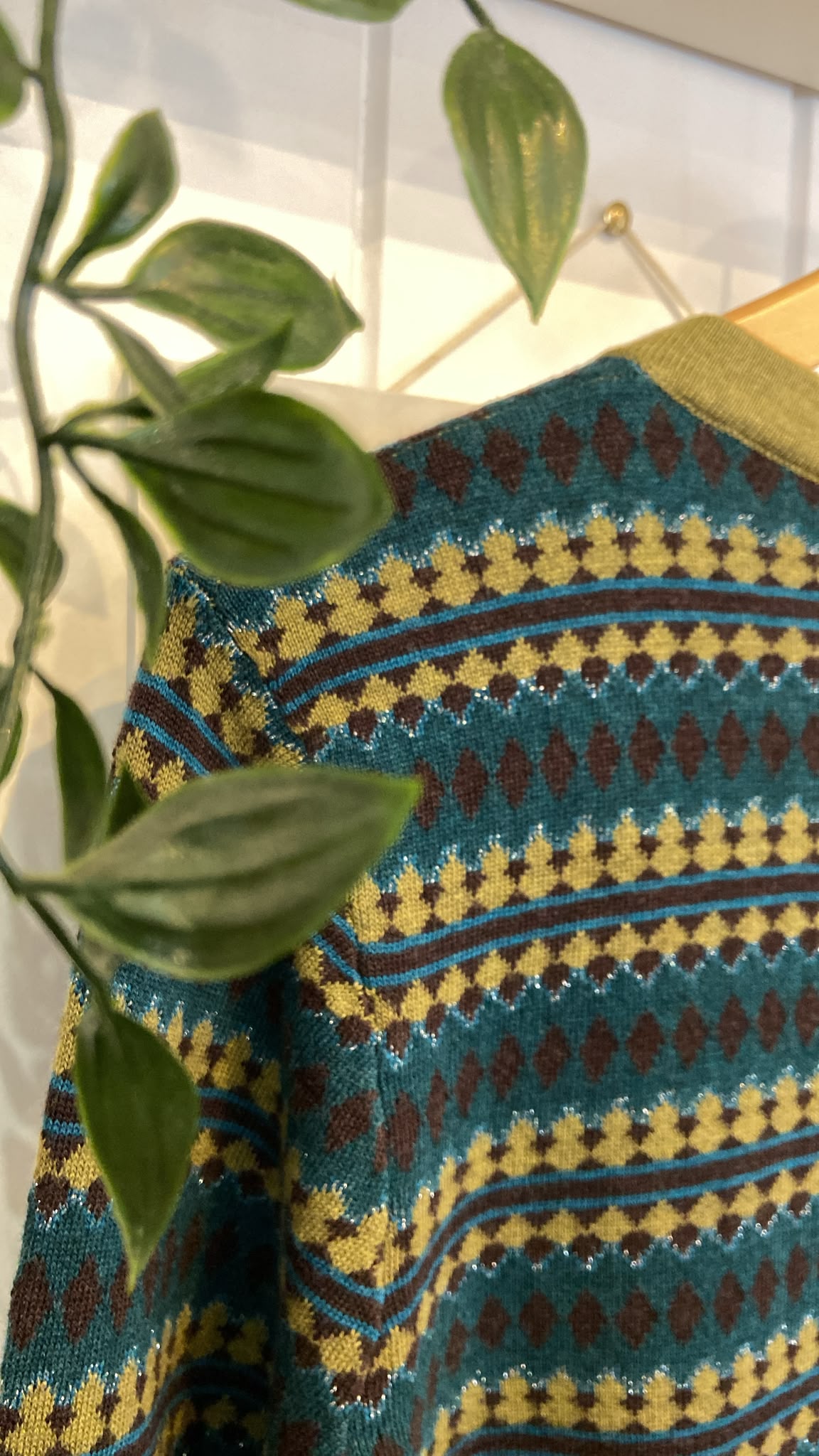 Close-up of a teal and olive fairisle patterned women's knit cardigan hanging on a wooden hanger.