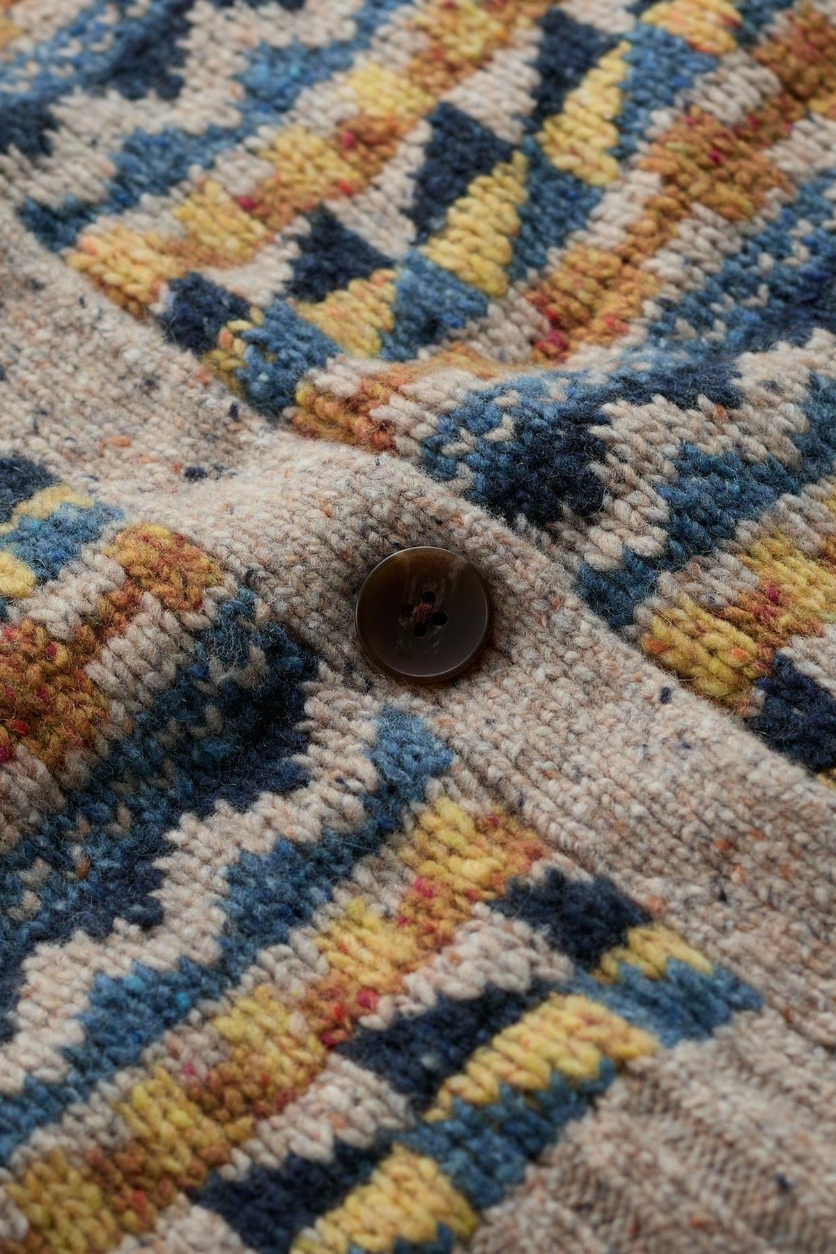 Close-up of a Fairisle pattern knit vest featuring a dark brown button and textured merino wool fabric.