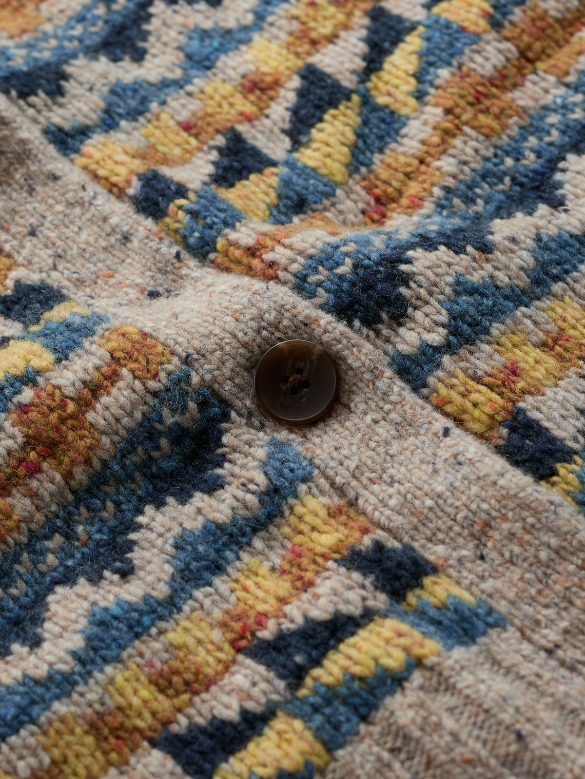 Close-up of a Fairisle pattern knit vest featuring a dark brown button and textured merino wool fabric.