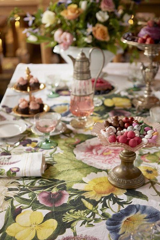Decorative table setting with floral tablecloth, pastries, and floral arrangements.