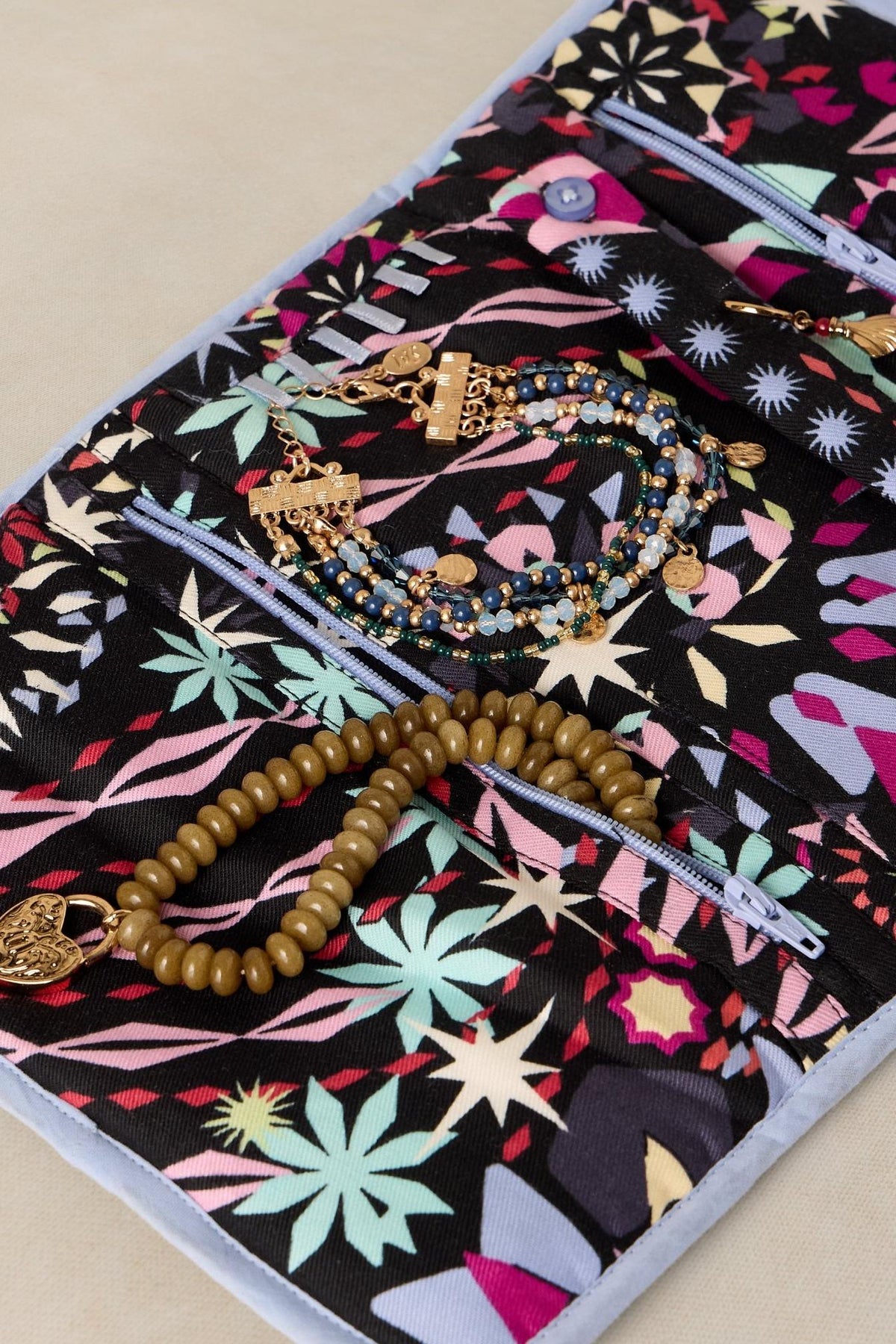 A patterned fabric jewellery organiser containing gold necklaces and beaded bracelets.