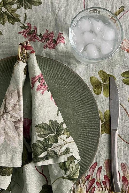 Table setting with floral napkins, plates, and a glass of water on a patterned tablecloth.