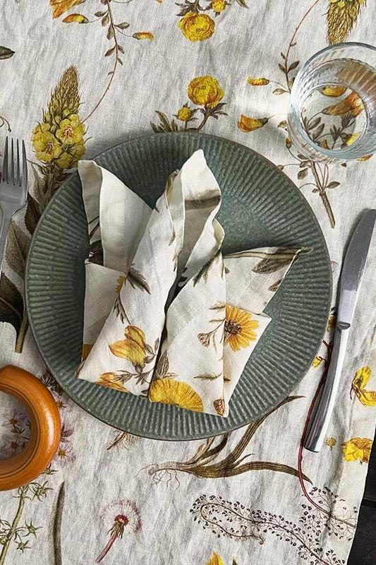 Table setting with floral tablecloth, green plate, silverware, and decorative items.