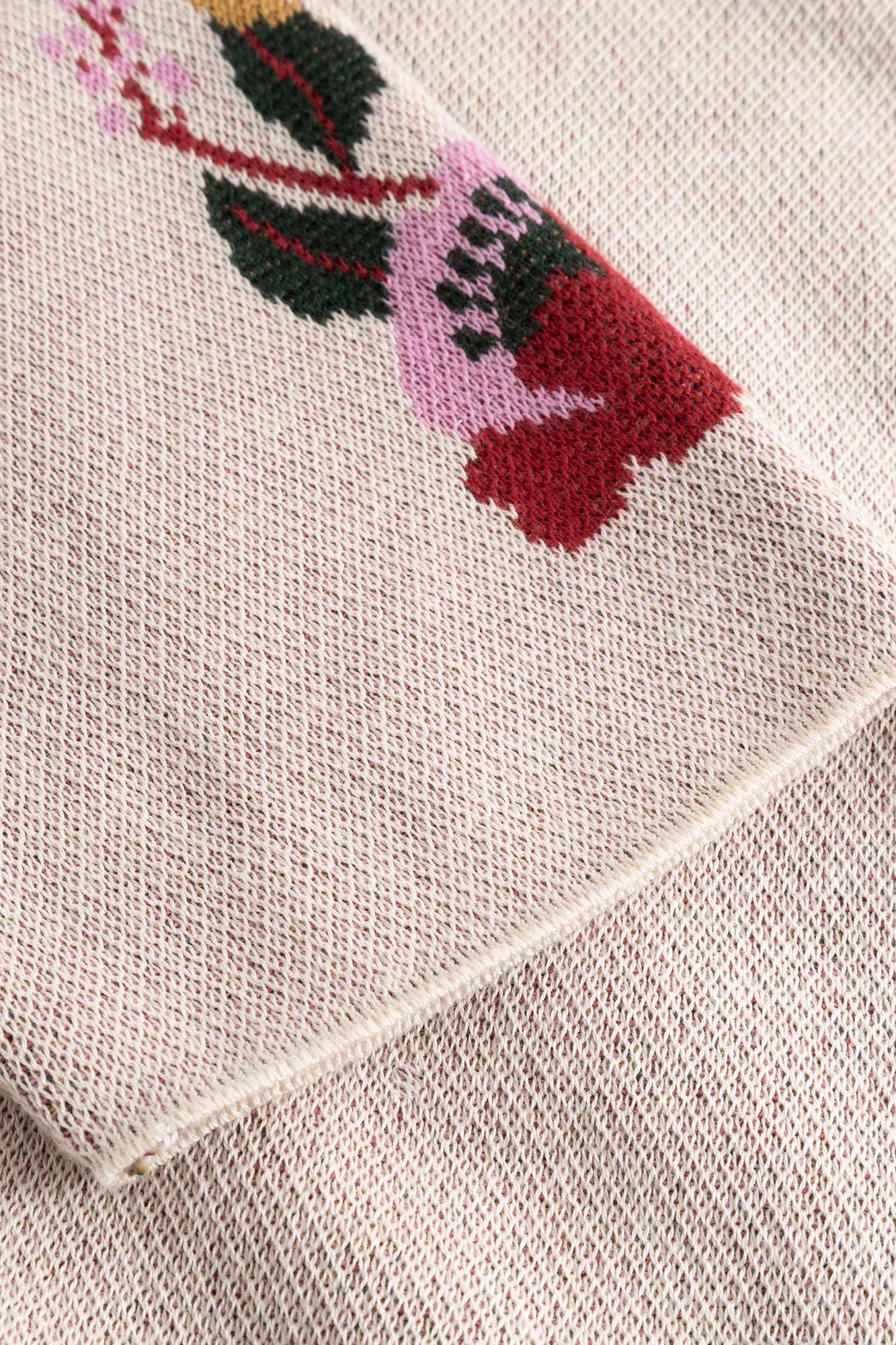Close-up of a cream-colored knit fabric with a colorful embroidered floral pattern in pink, red, green, and yellow.