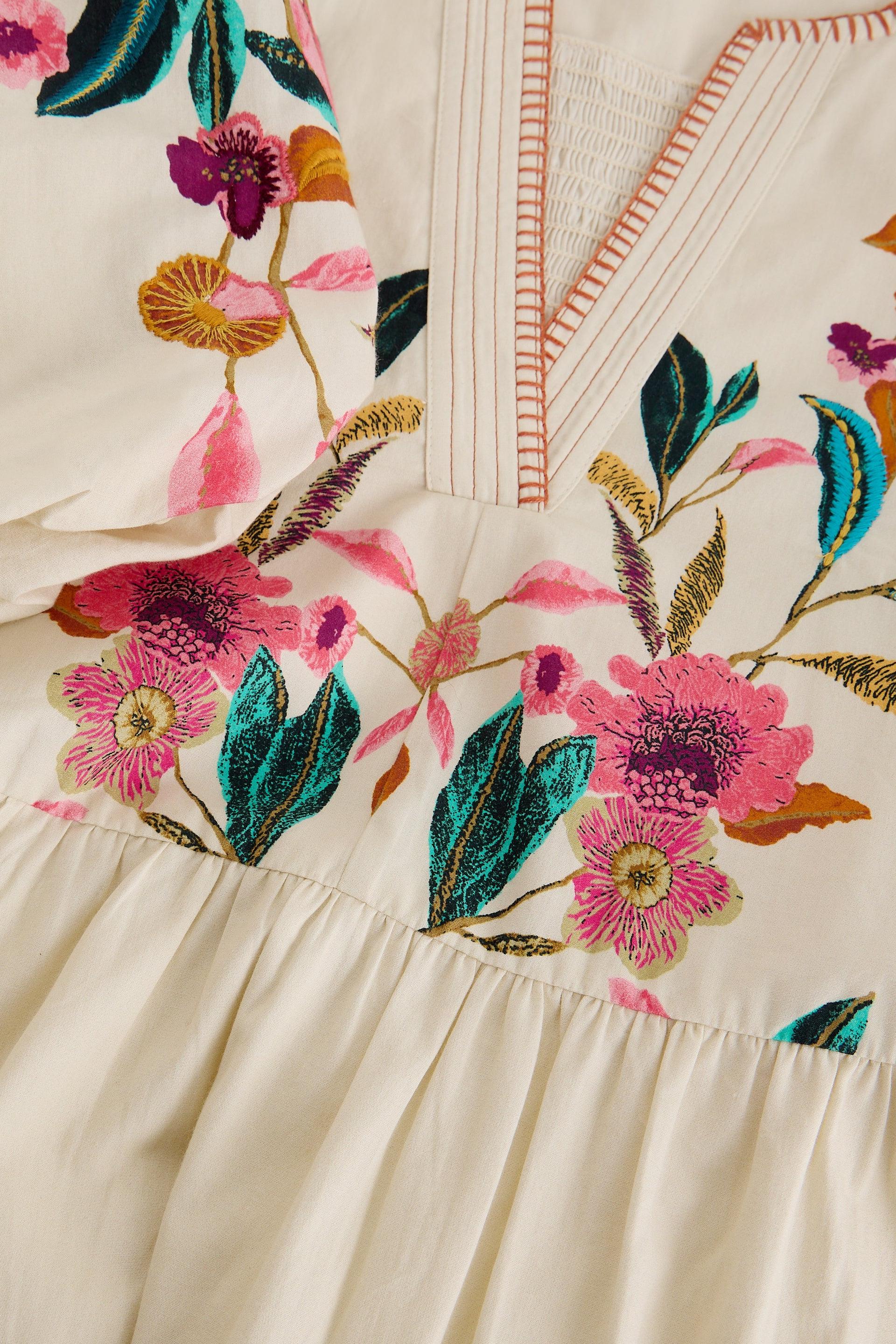Close-up of a cream-colored occasion dress with vibrant floral embroidery and smocked neckline.
