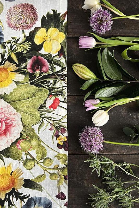 Floral table runner on the left and real flowers on a wooden surface on the right.