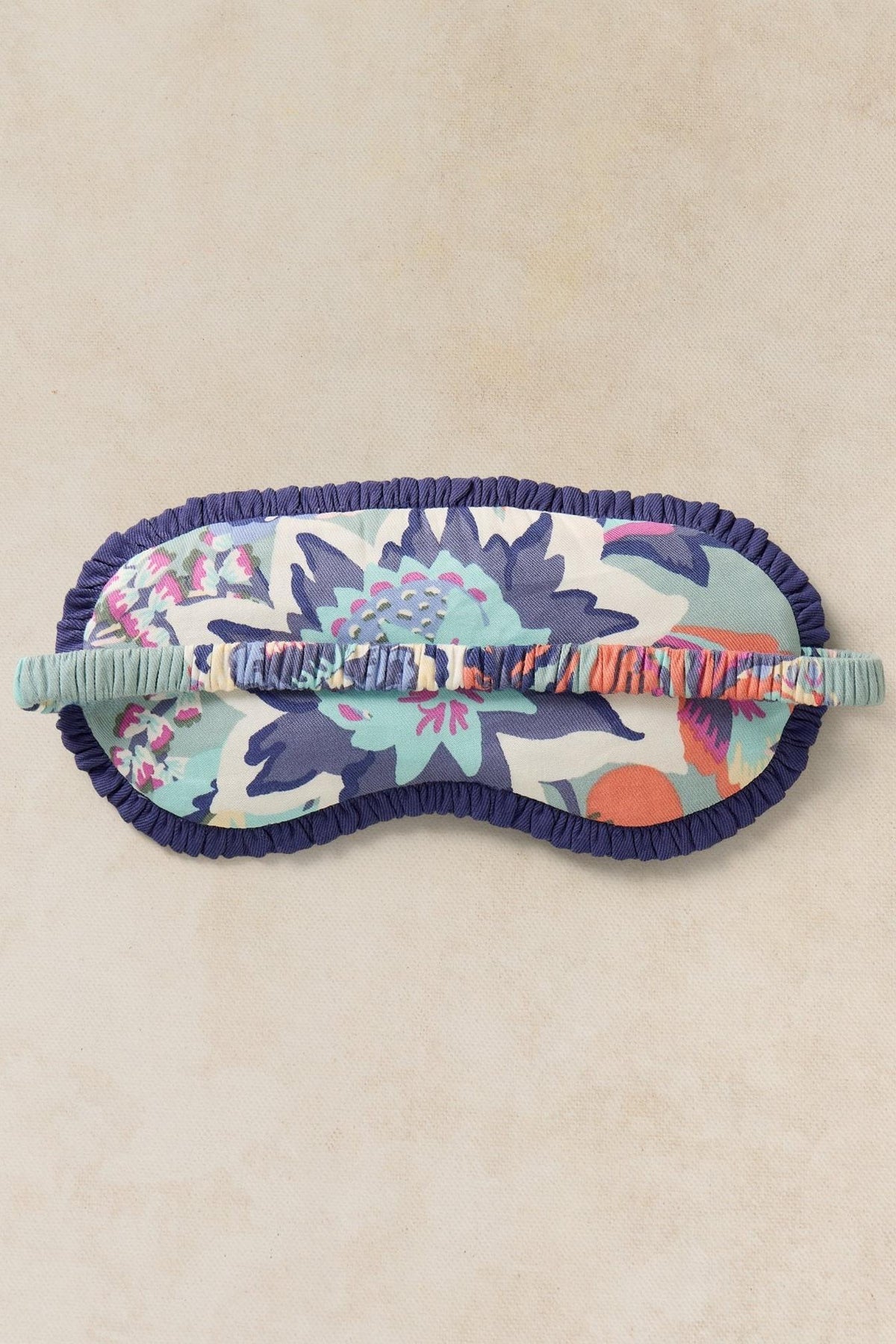 White Stuff floral print sleep mask for women with a dark blue ruffled trim on a neutral background.