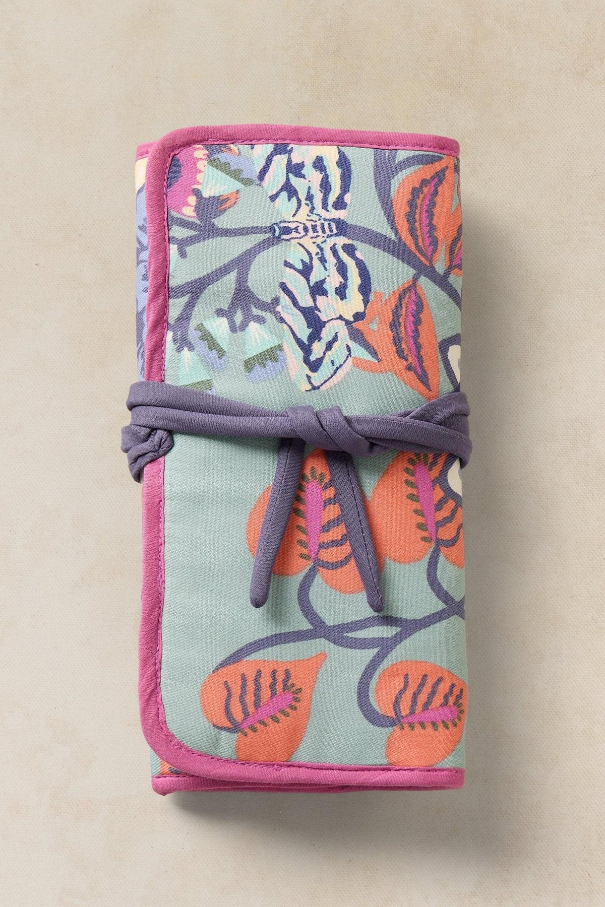 Floral patterned travel jewellery organiser pouch tied with a purple ribbon on a plain background.