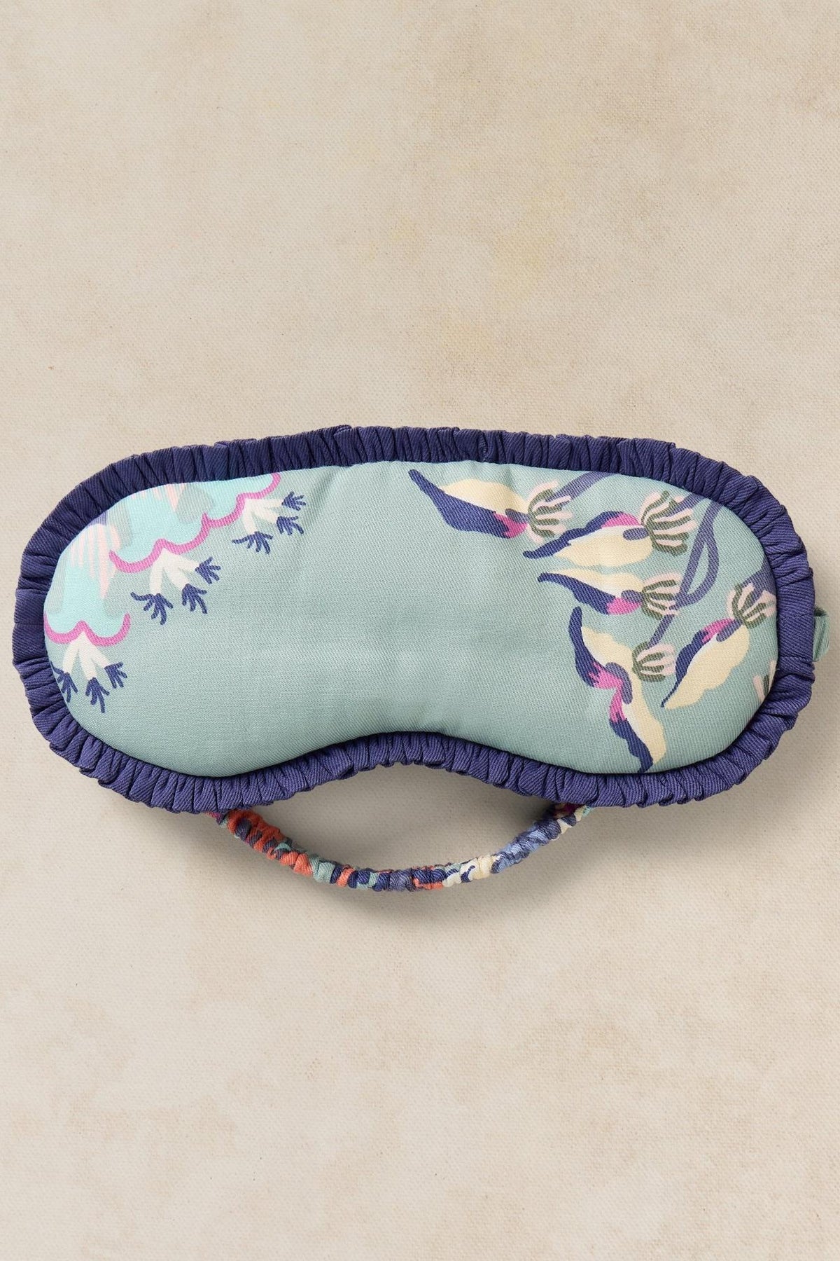 A floral print fabric sleep mask for women with navy ruffled edges on a neutral background.