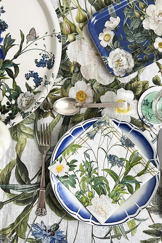 Floral and botanical table setting with plates, cutlery, and glasses on a matching tablecloth.