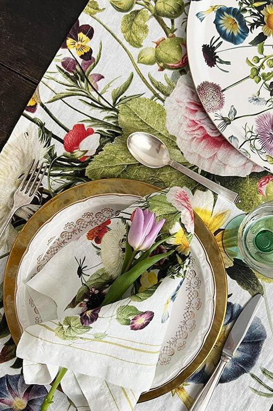Table setting with floral-patterned plates, cloth napkins, and cutlery on a matching tablecloth.