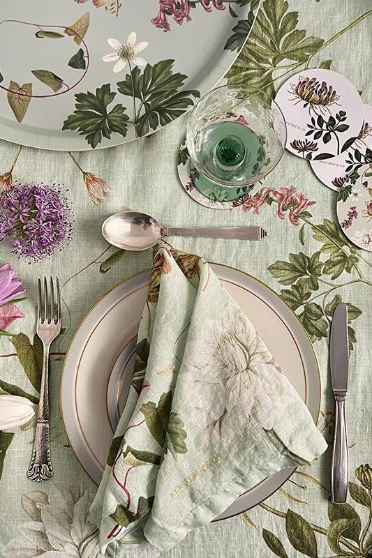 Table setting with floral tablecloth, plates, cutlery, and napkins on a wooden surface.