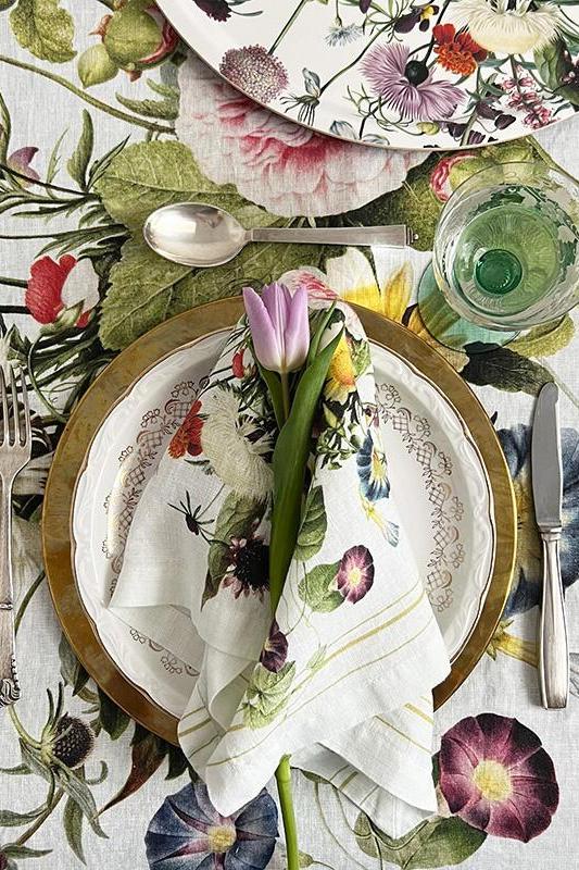 Table setting with floral and nature-themed tablecloth, plates, and cutlery on a wooden surface.