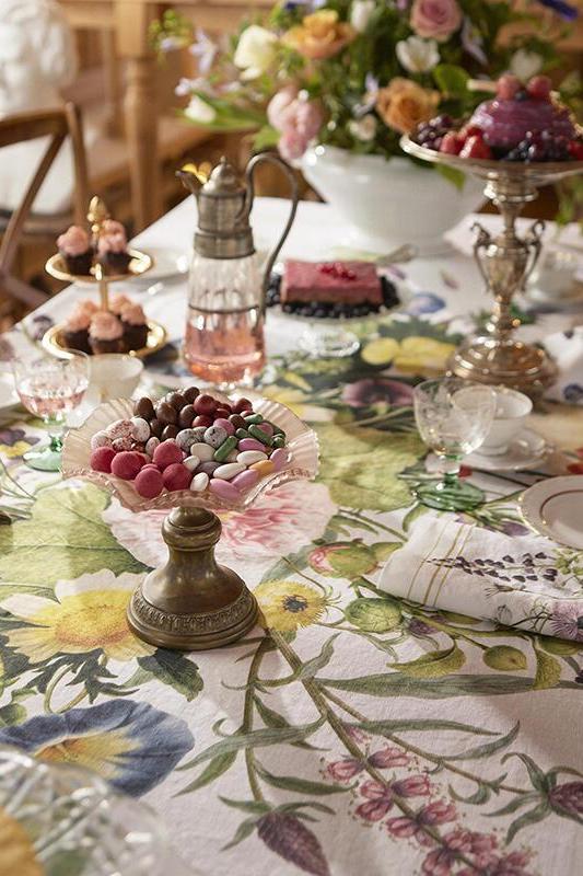 Decorative table setting with floral tablecloth, pastries, and silver teapots.