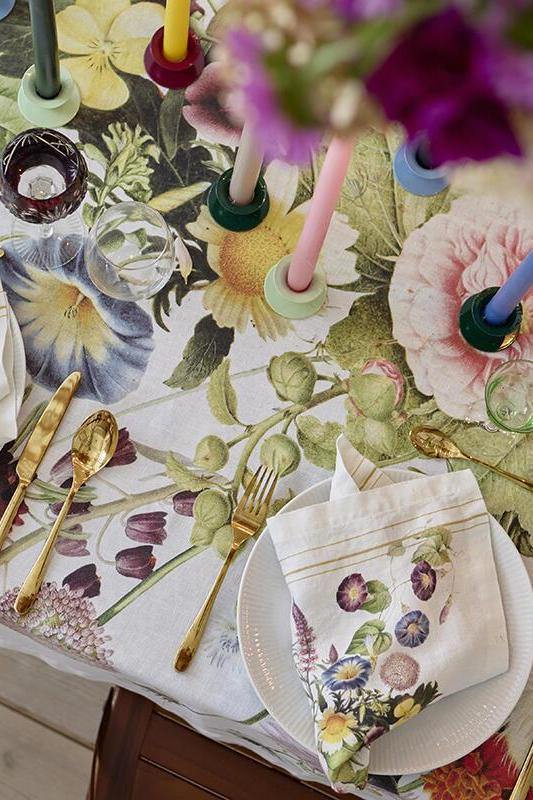 Decorative table setting with floral tablecloth, cutlery, and candles on a wooden table.