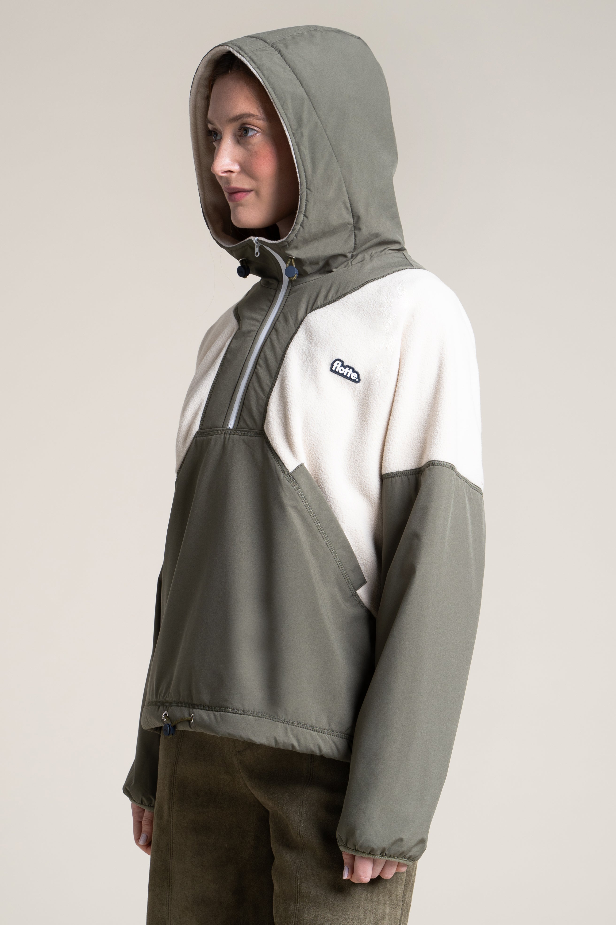 A model wears a two-tone olive green and cream recycled polyester pull-over coat from the European brand Flotte.
