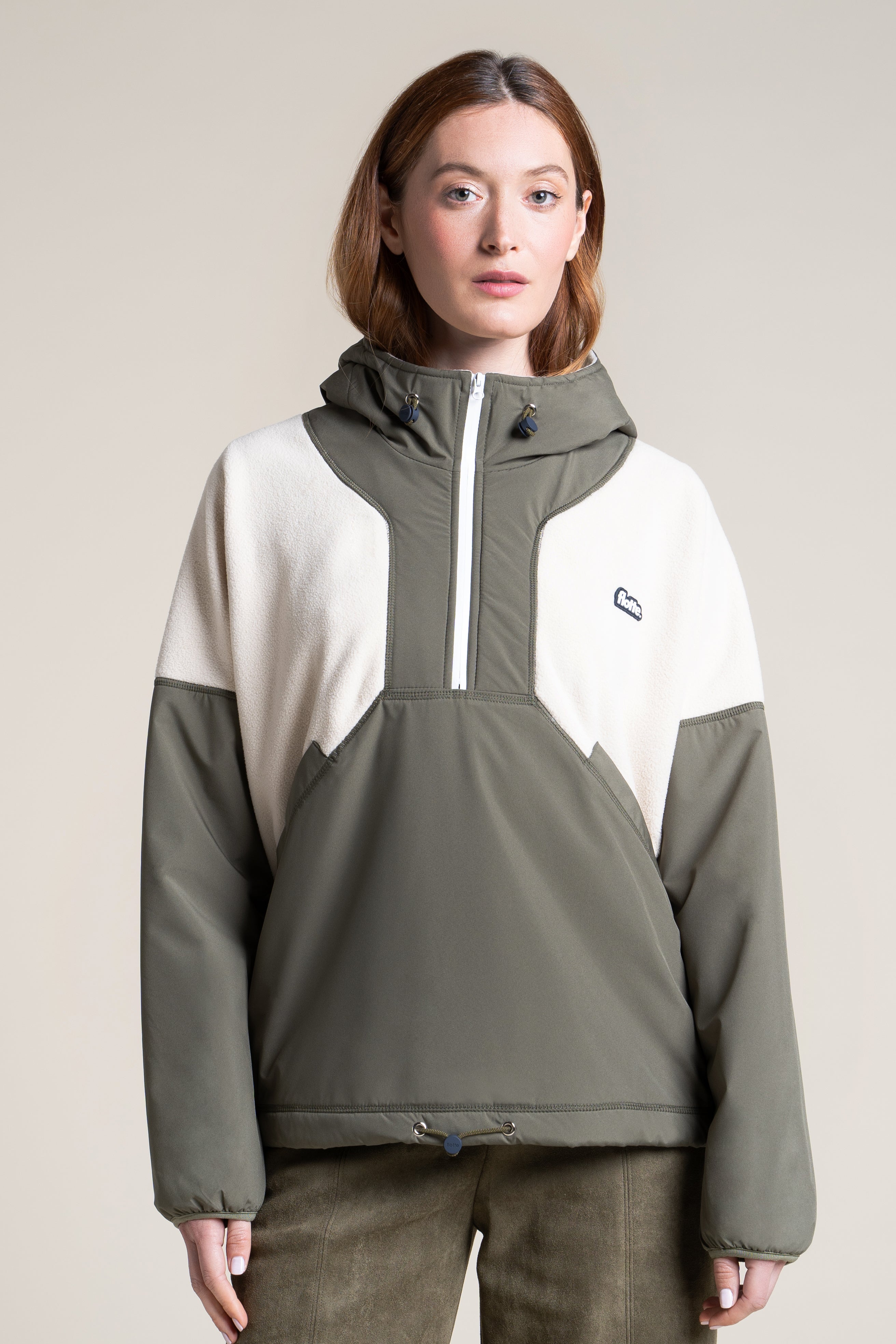 A person wearing a khaki and cream recycled polyester pull-over waterproof coat by Flotte.