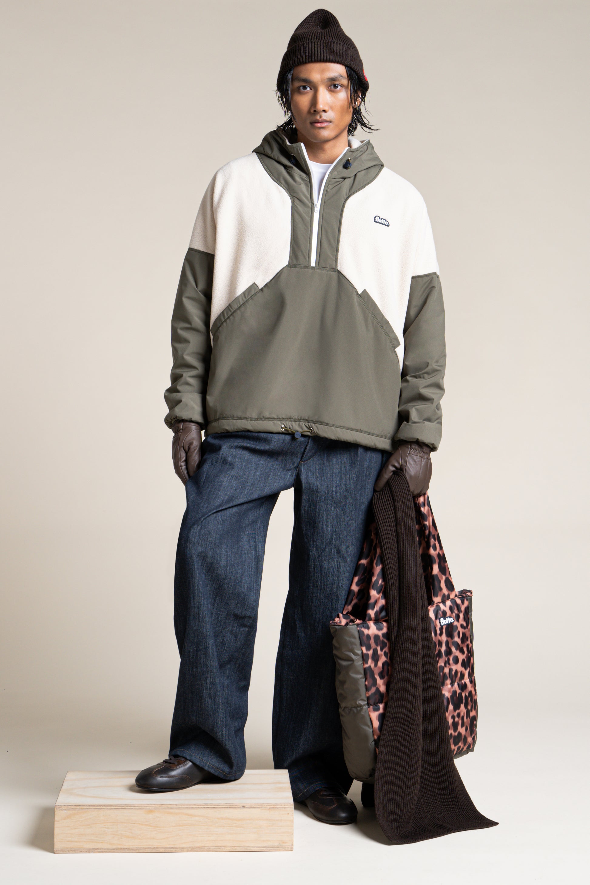 A person wearing a colour-blocked olive and cream Flotte pull-over coat made from recycled polyester.