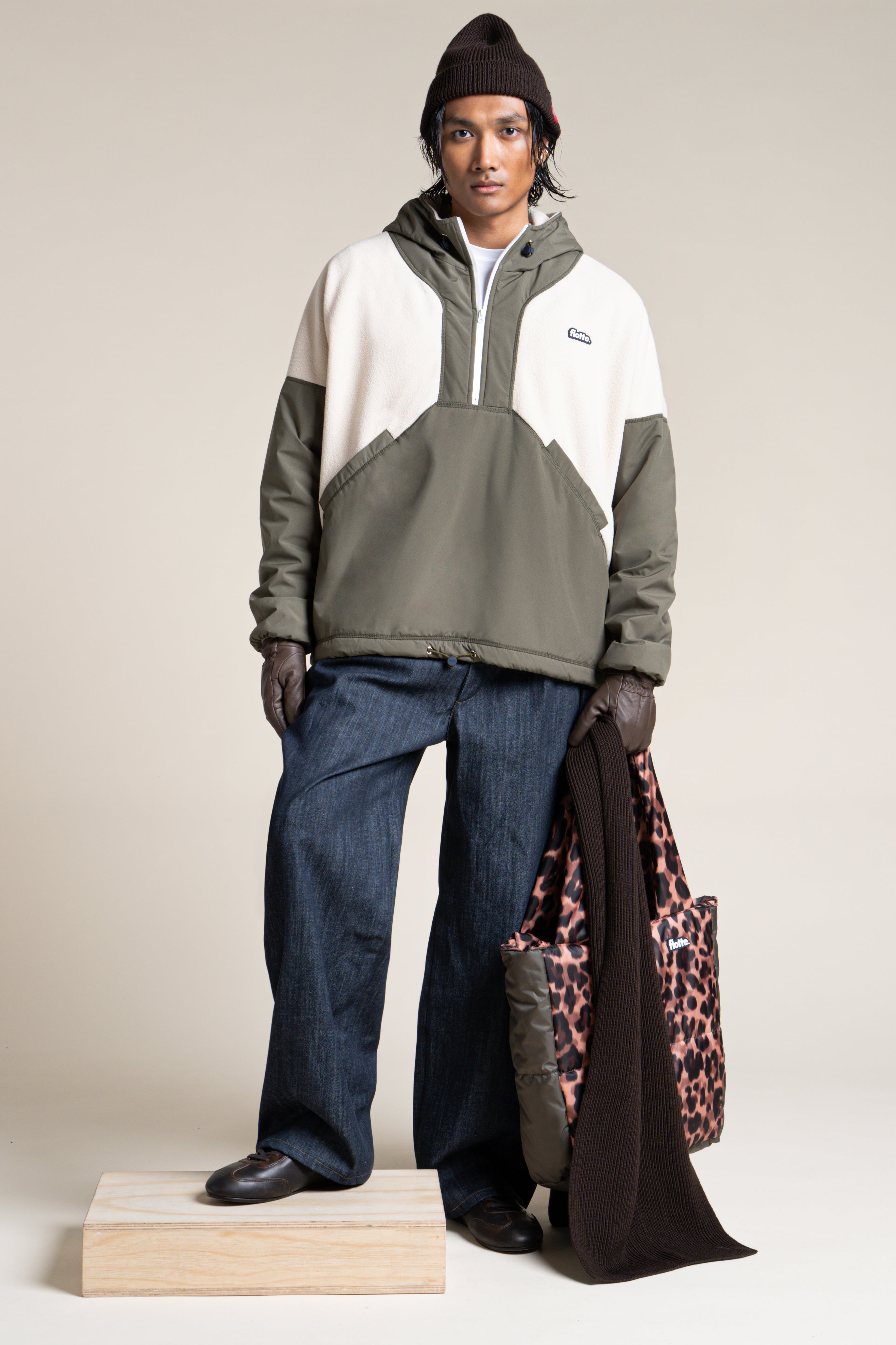 A person wearing a colour-blocked olive and cream Flotte pull-over coat made from recycled polyester.