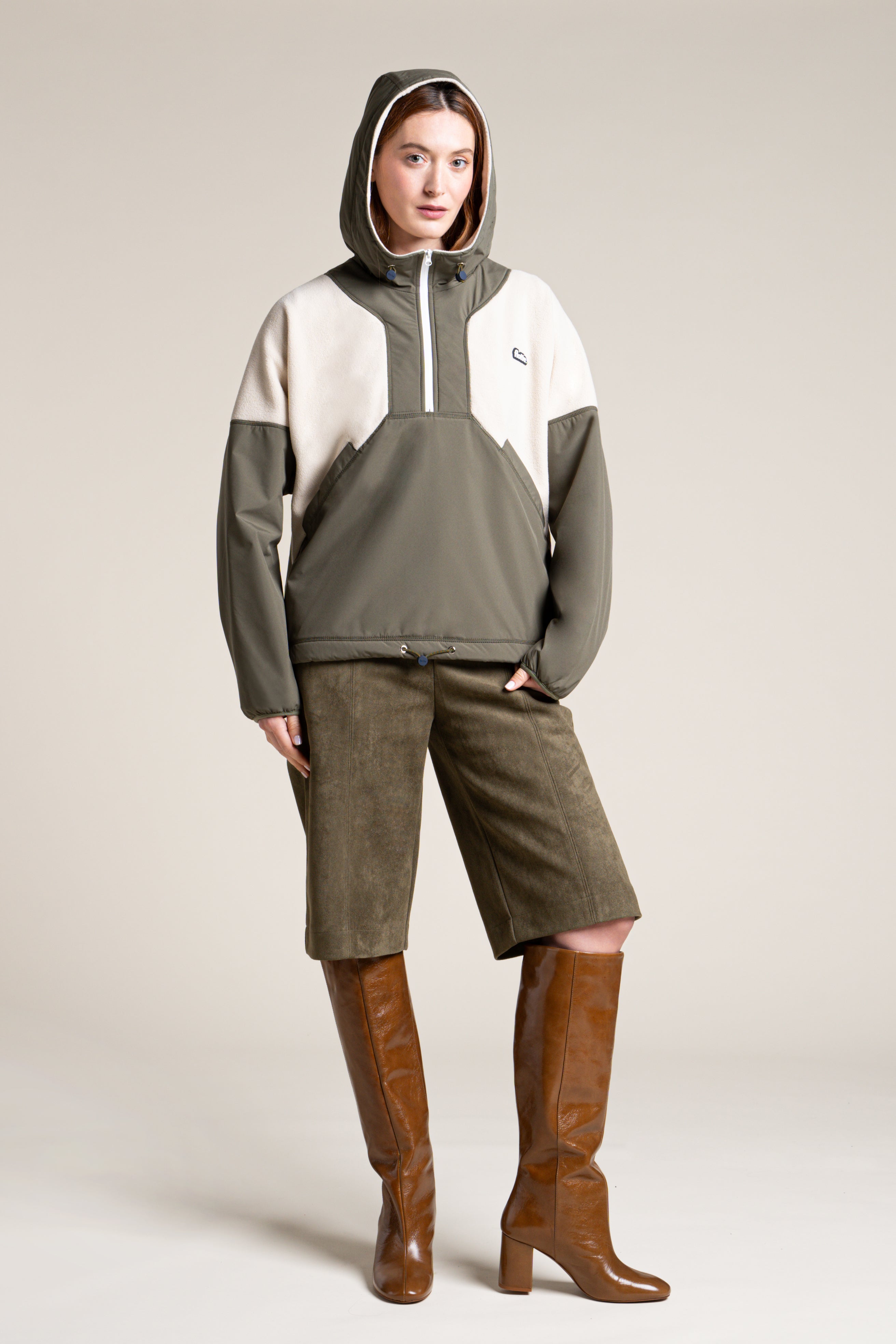 Woman wearing a hooded olive and cream recycled polyester unisex pull-over coat against a neutral background.