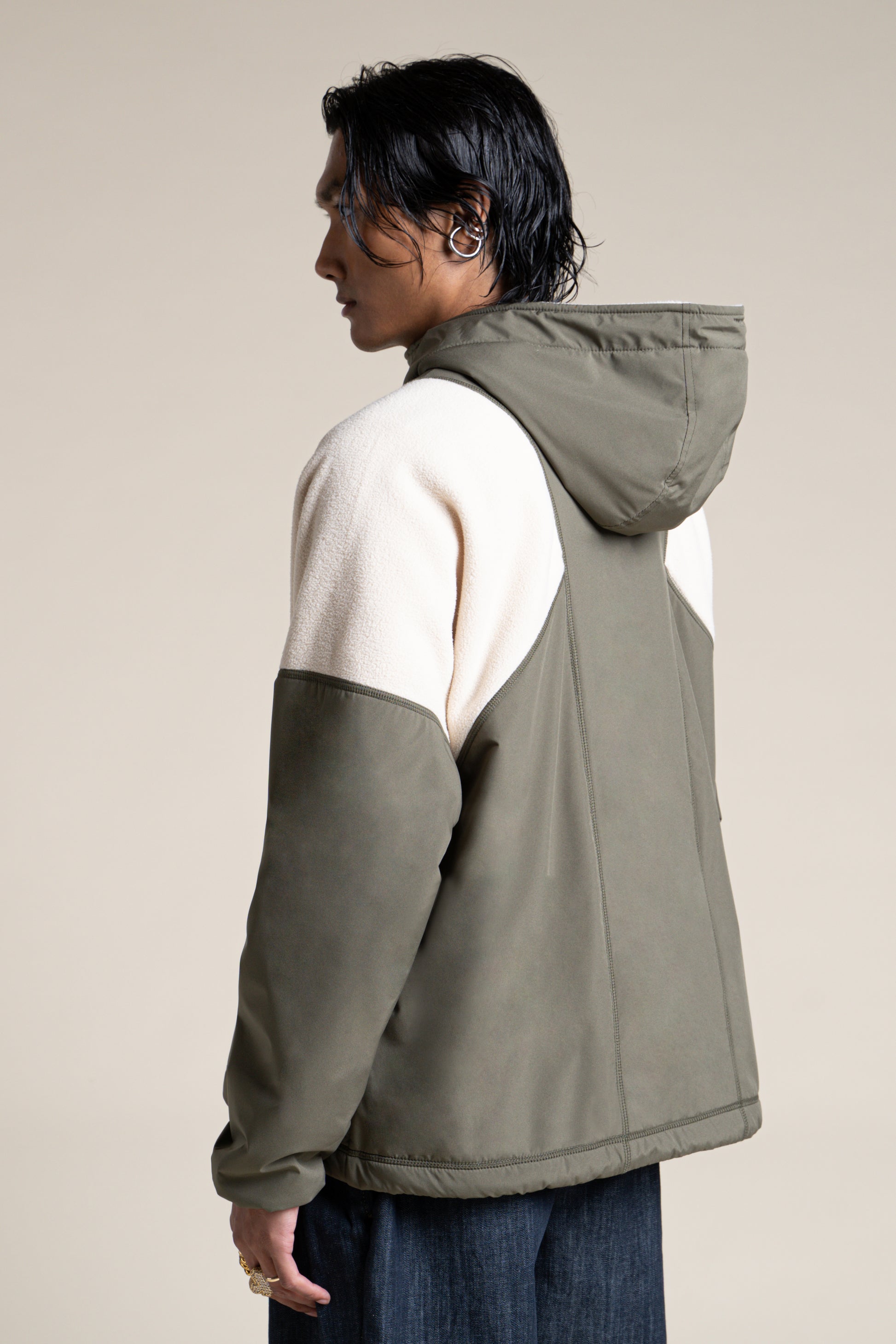 A person wearing a two-tone olive green and cream recycled polyester unisex pullover coat from Flotte.