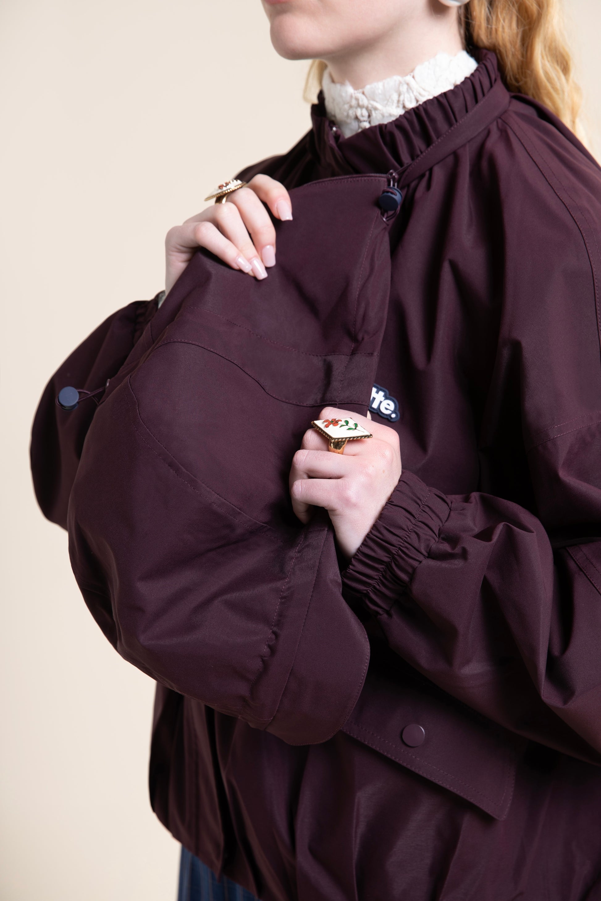Person wearing a stylish maroon Flotte waterproof coat over a white lace collar shirt