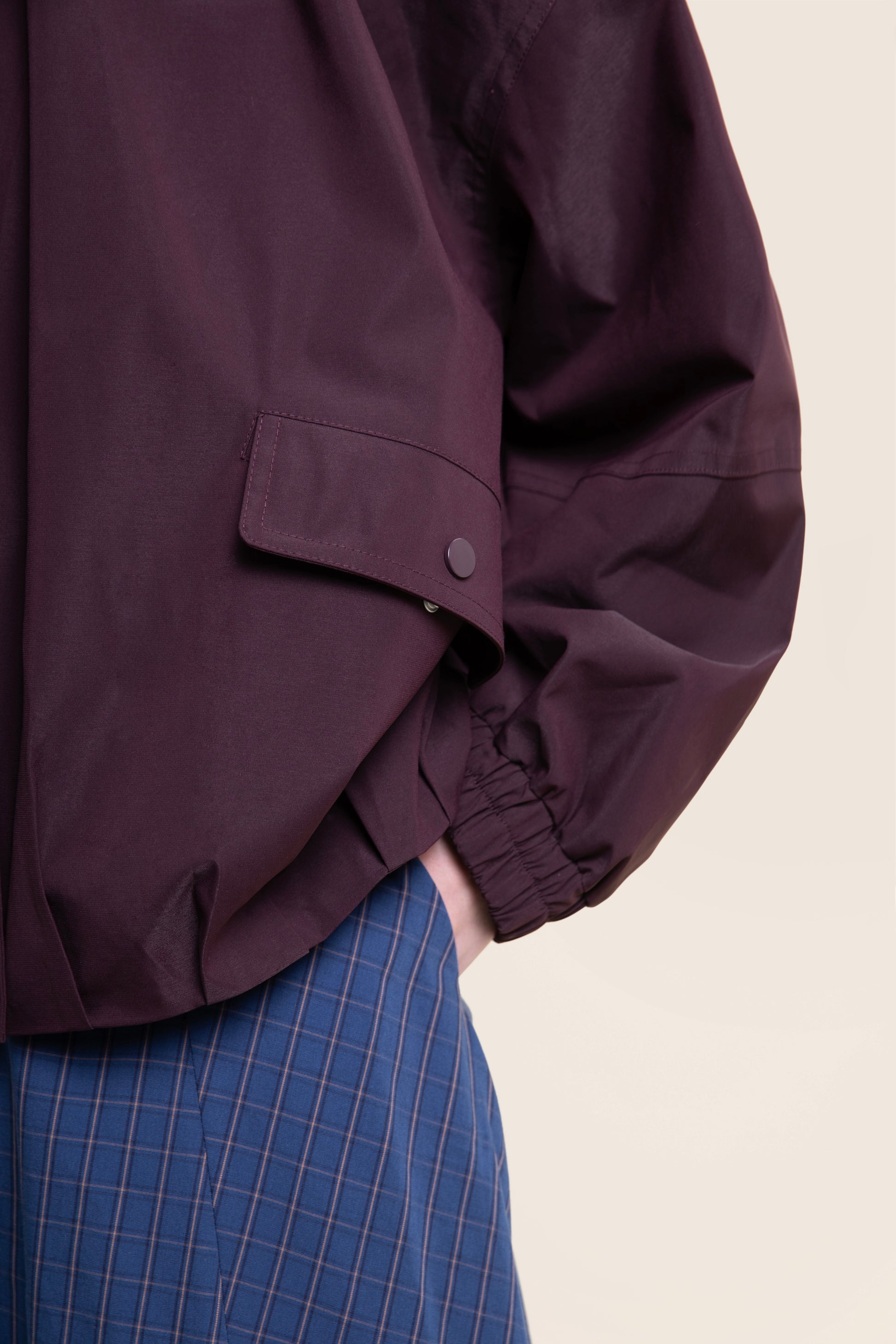 Close-up of a maroon waterproof coat featuring a flap pocket and elasticated cuffs.