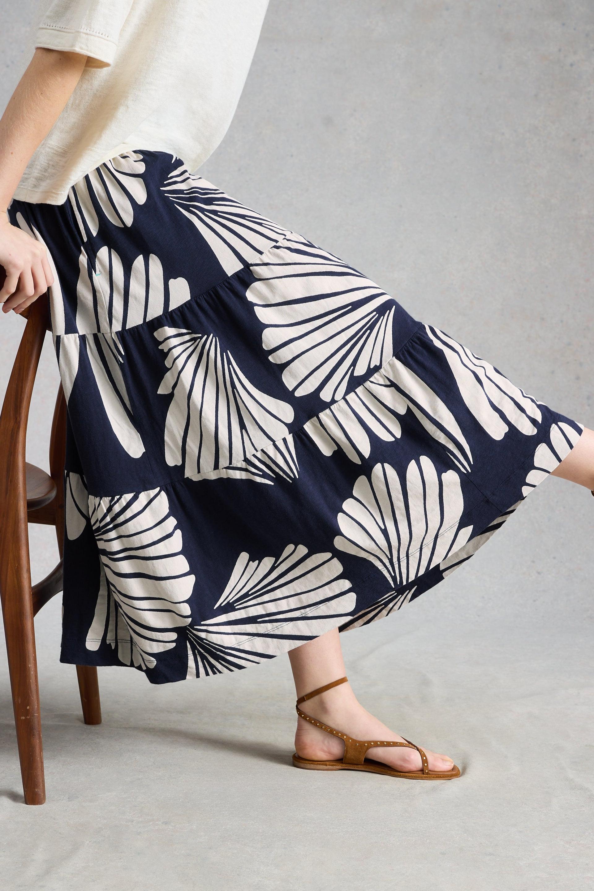 Woman wearing a navy blue skirt with white leaf pattern sitting on a chair.